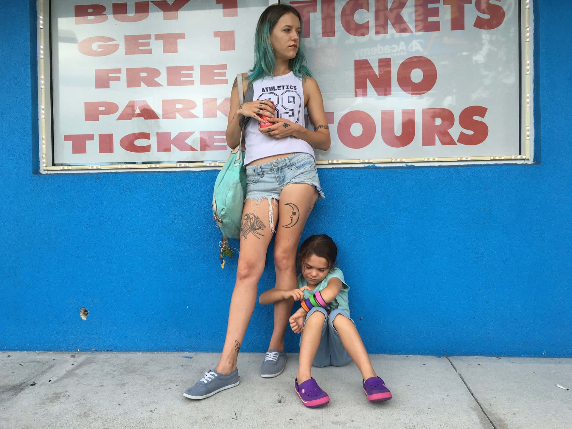  壁紙 — 一位擁有藍綠色頭髮的女人和一個孩子坐在明亮的藍色牆壁下，旁邊有一個褪色的停車罰單標誌。