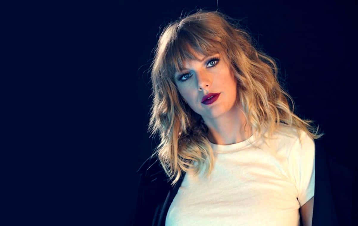 Taylor Swift Lover 桌布 壁紙 — 一位擁有波浪形金髮和大膽紅唇的女性，在深藍色背景下凝視著。