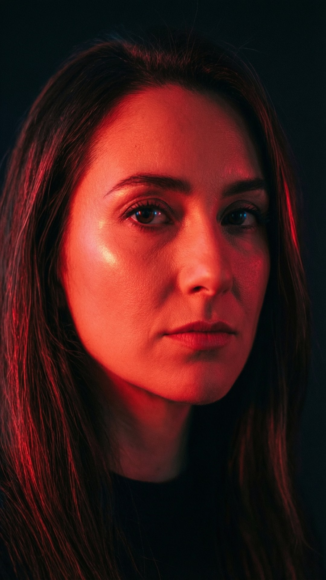 Neon Portrait 壁紙 — 一位女性的臉龐在黑暗背景下被強烈的紅光籠罩，她的目光直接而強烈。