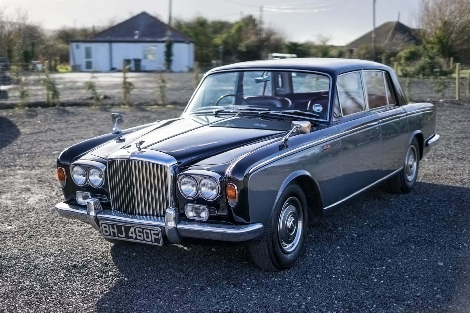 Bentley T1 桌布 壁紙 — 一架時尚的黑色復古賓利轎車在明亮的陽光下閃閃發光，停在碎石地上，背景是一座白色房子。