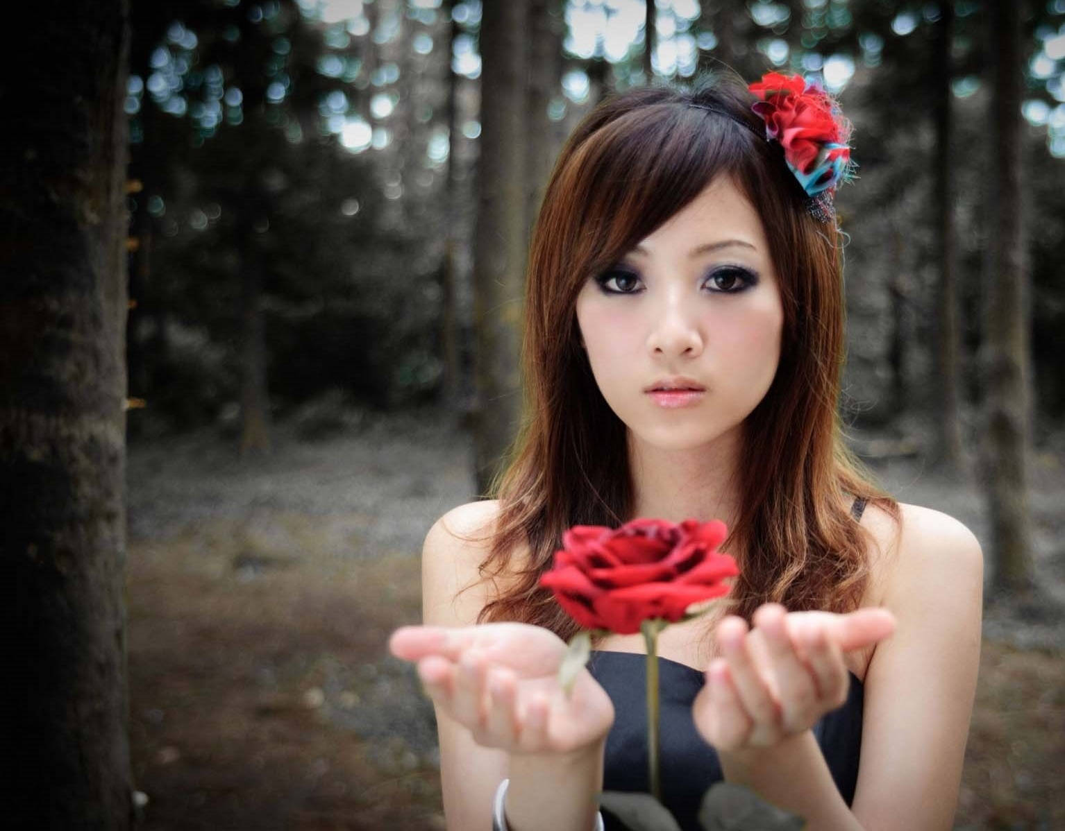 一位女性在森林中，雙手捧著一朵紅玫瑰。