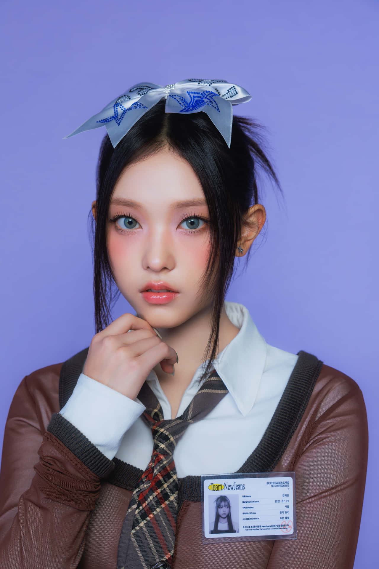  壁紙 — 一位身穿校服、佩戴藍色蝴蝶結和身份證徽章的年輕女性，在純紫色背景前擺姿勢。