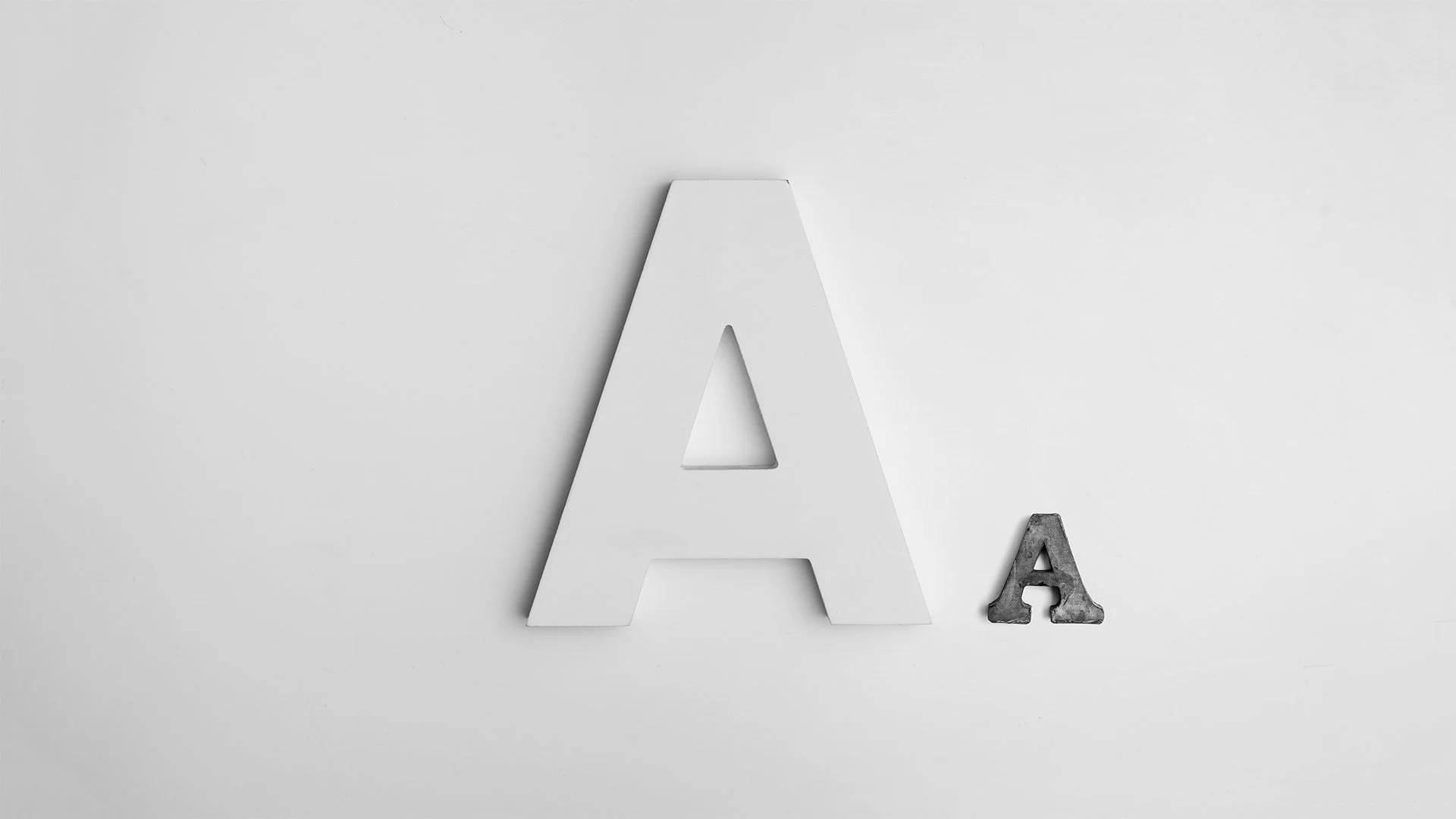 純白背景字母A 壁紙 — 一個白色大寫字母A旁邊有一個細小風化的小寫字母a，位於純淺灰色表面上。