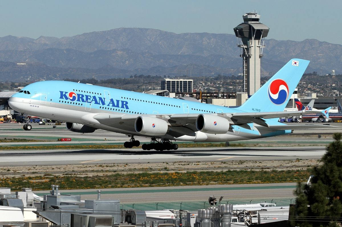 韓亞航空A380-800停泊機場 壁紙 — 一架大韓航空空中巴士A380在晴朗天空下滑行在跑道上，背景有山脈和機場控制塔。