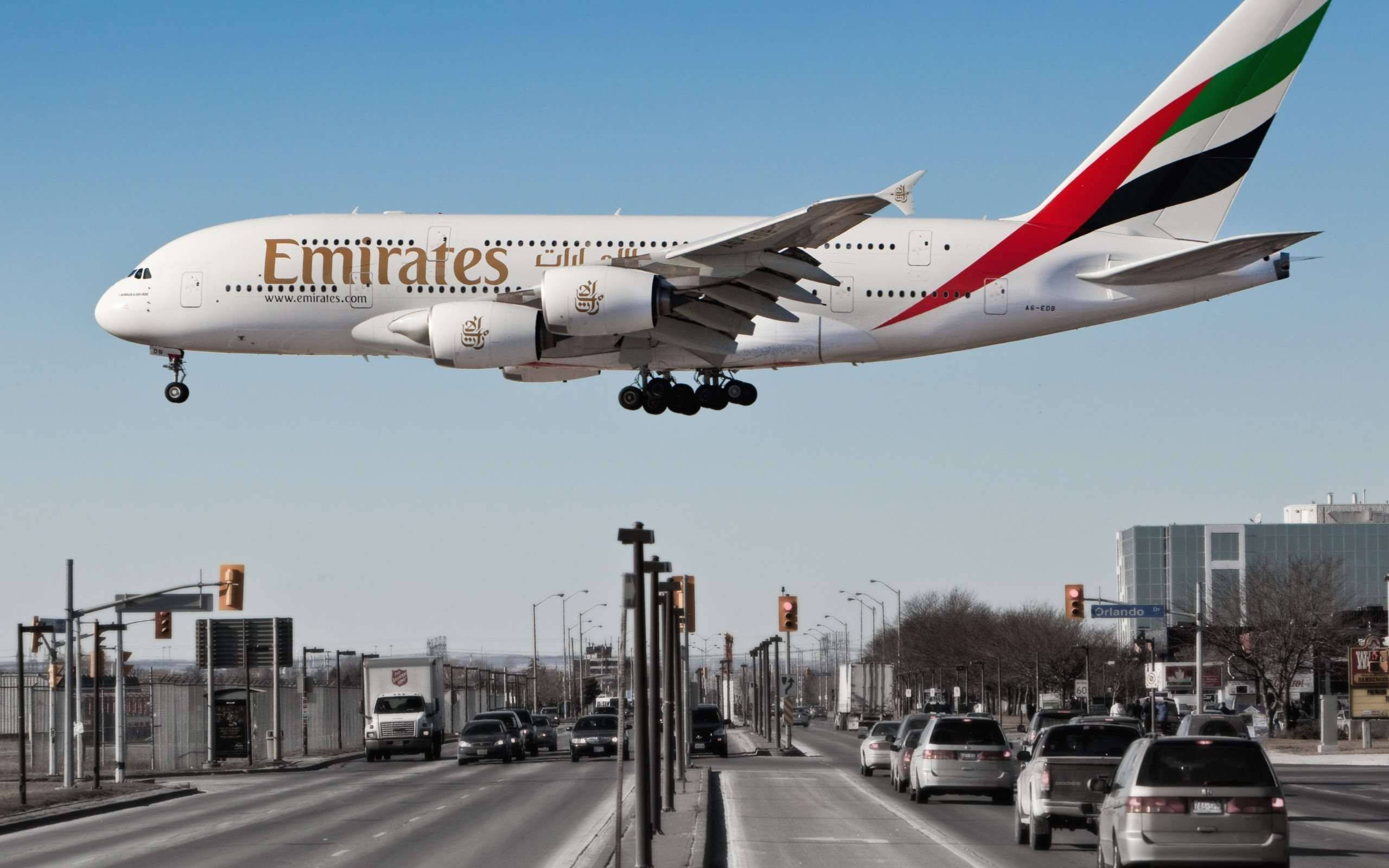 阿聯酋A380飛越雪梨 壁紙 — 一架阿聯酋航空空中巴士A380低飛過繁忙的城市高速公路，下方有汽車和交通燈。