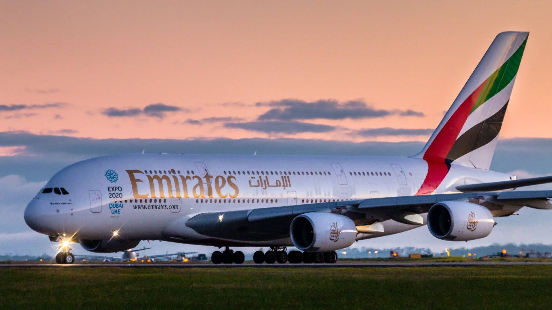 阿聯酋航空A380雙層客機模型 壁紙 — 一架大型阿聯酋航空空中巴士A380在黃昏時分在跑道上滑行，背後是粉紅色和橙色的天空。