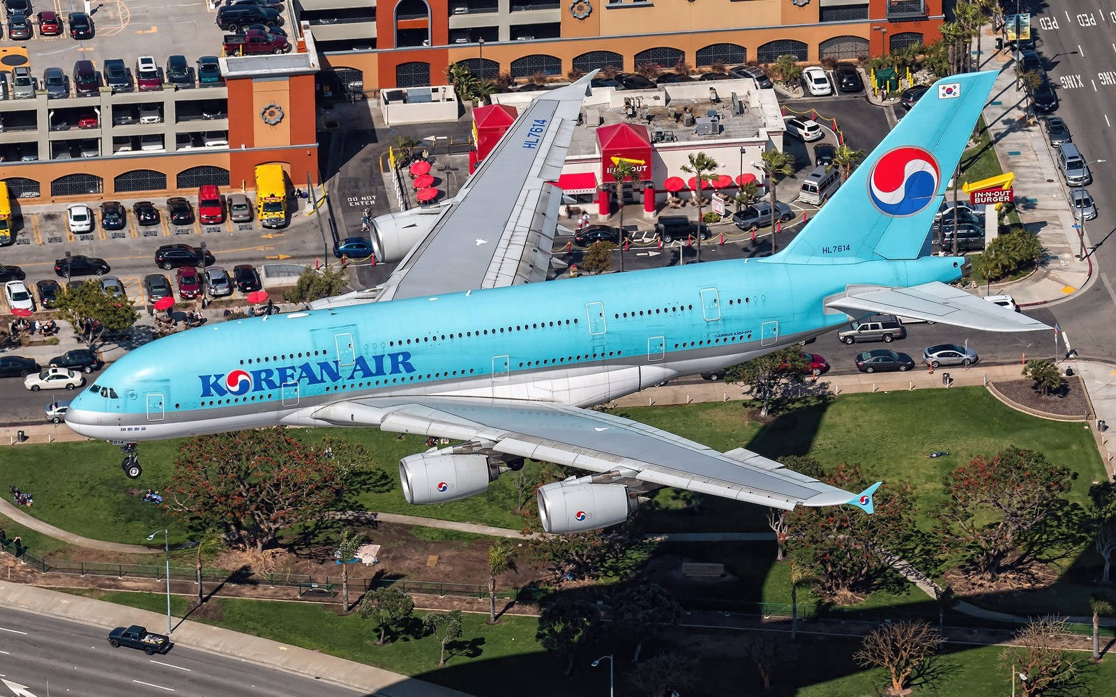 韓亞航空A380飛越加州 壁紙 — 一架淺藍色塗裝的大韓航空空中巴士A380在陽光普照的城市景觀上空低飛，下方有停車場和建築物。