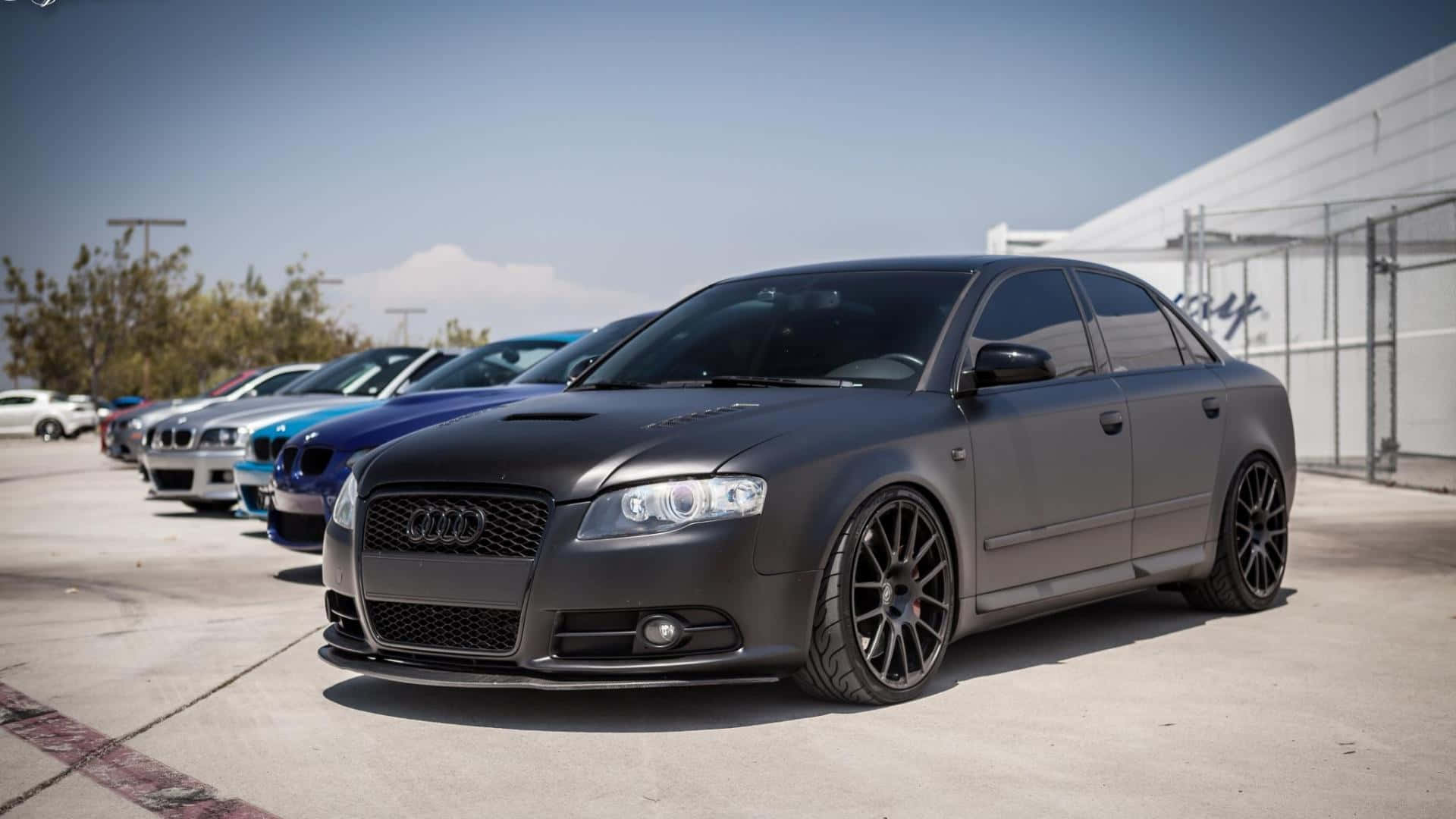 Audi Rs4 桌布 壁紙 — 一架啞黑色奧迪房車配備訂製輪圈，在明亮日光下排成一列停泊。