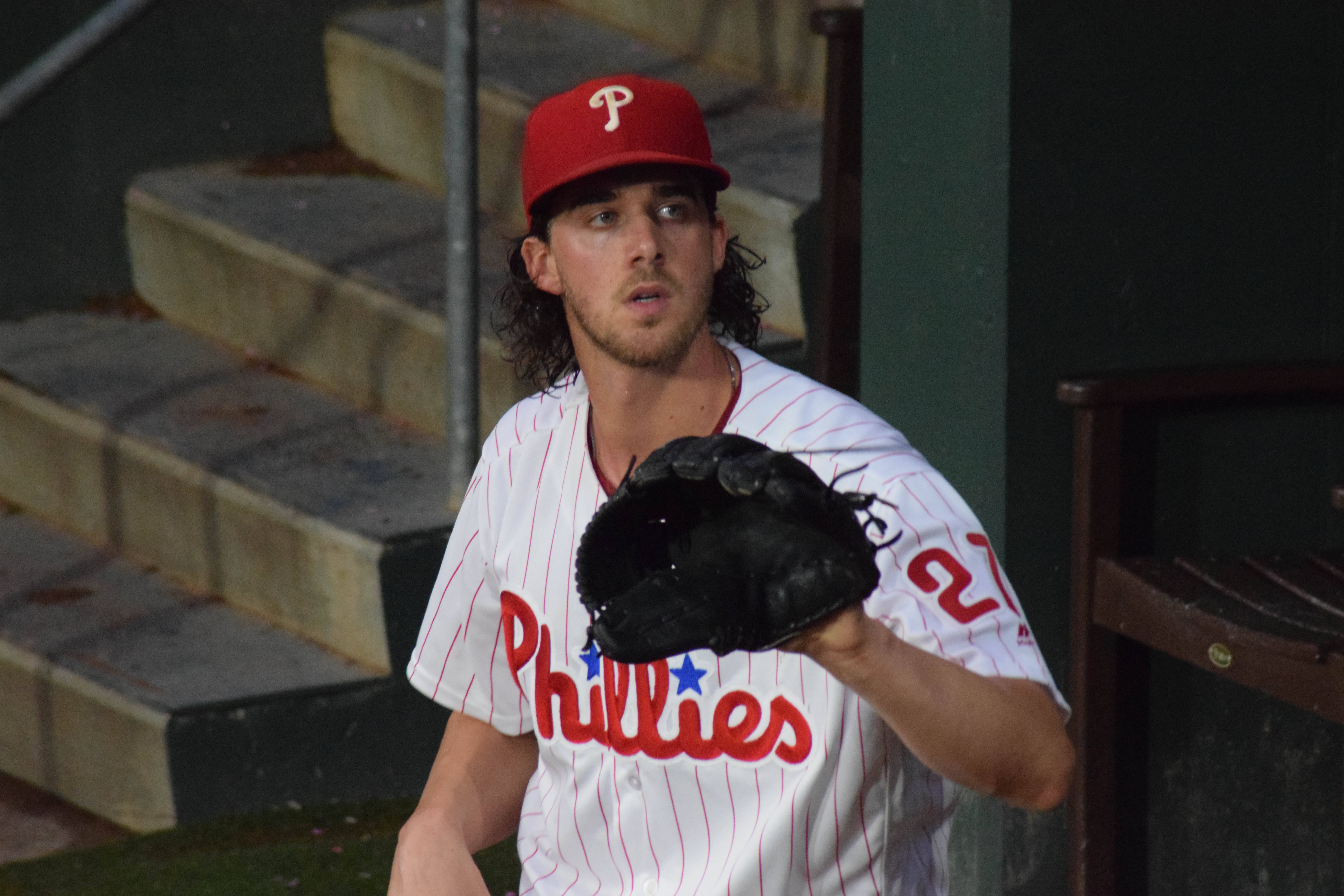Aaron Nola 拿手套 壁紙 — 一位費城費城人棒球運動員穿著細條紋制服，站在球員休息區，手持手套。