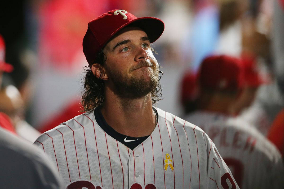 Aaron Nola 做OK手勢 壁紙 — 一名戴紅色帽、身穿條紋球衣的棒球運動員在比賽中抬頭仰望，神情若有所思。