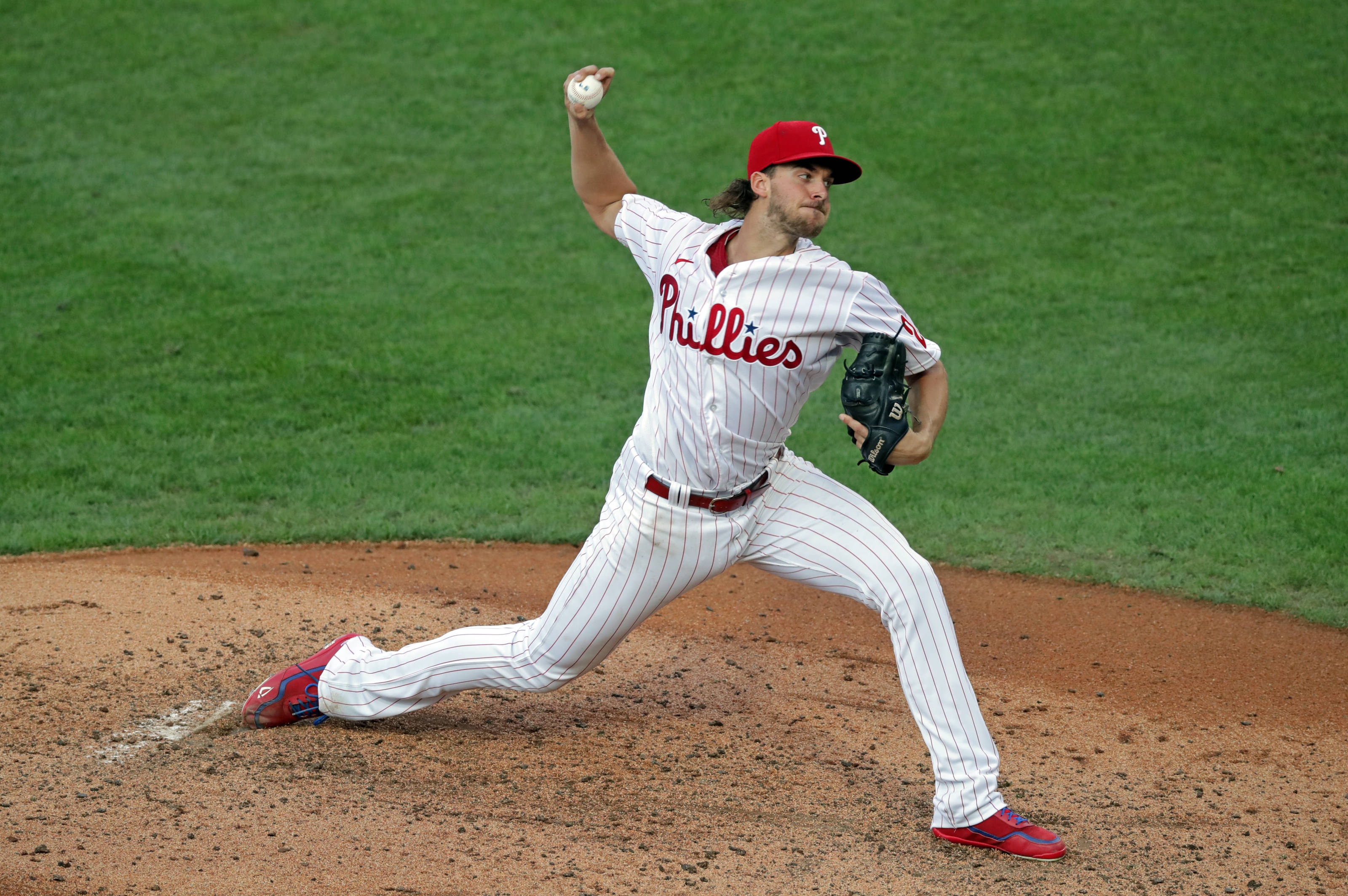 Aaron Nola 拋球 壁紙 — 費城人隊投手在球場燈光下，於綠色草地和棕色泥土的棒球投手丘上投球中。