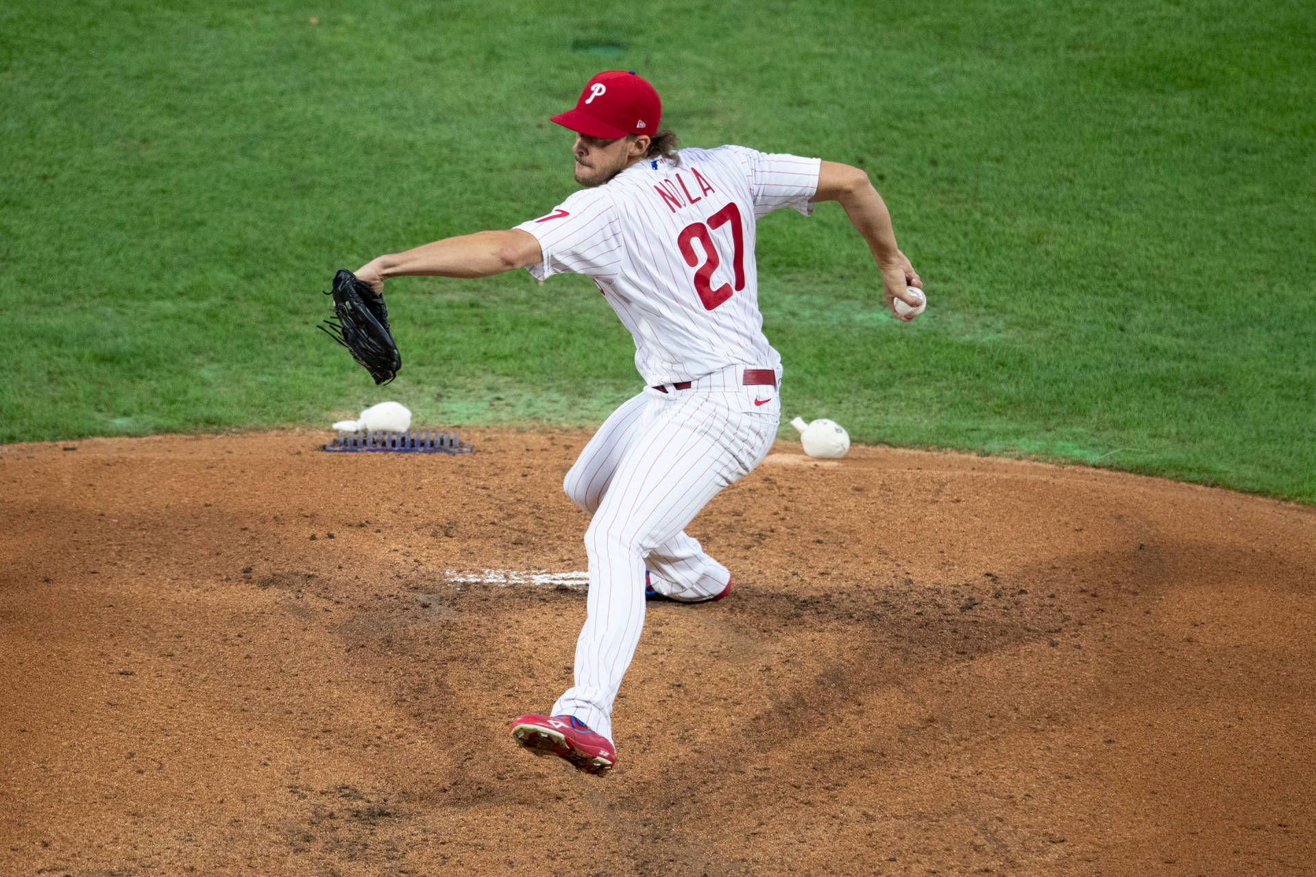 Aaron Nola 準備快速球 壁紙 — 一名身穿白色細條紋制服、戴紅色帽子、背號27的棒球投手，正在綠色球場的投手丘上投球。