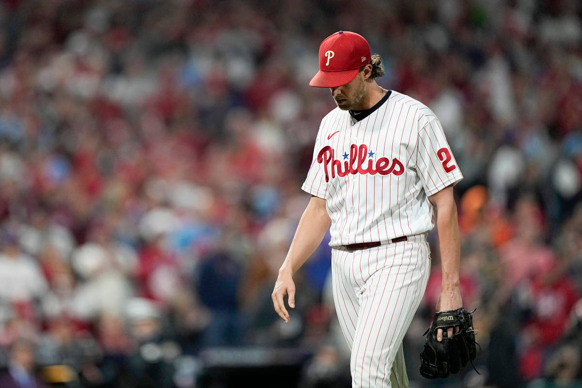 Aaron Nola 頭低垂 壁紙 — 一名身穿紅白球衣的費城費城人棒球運動員，手拿手套沮喪地離開球場。