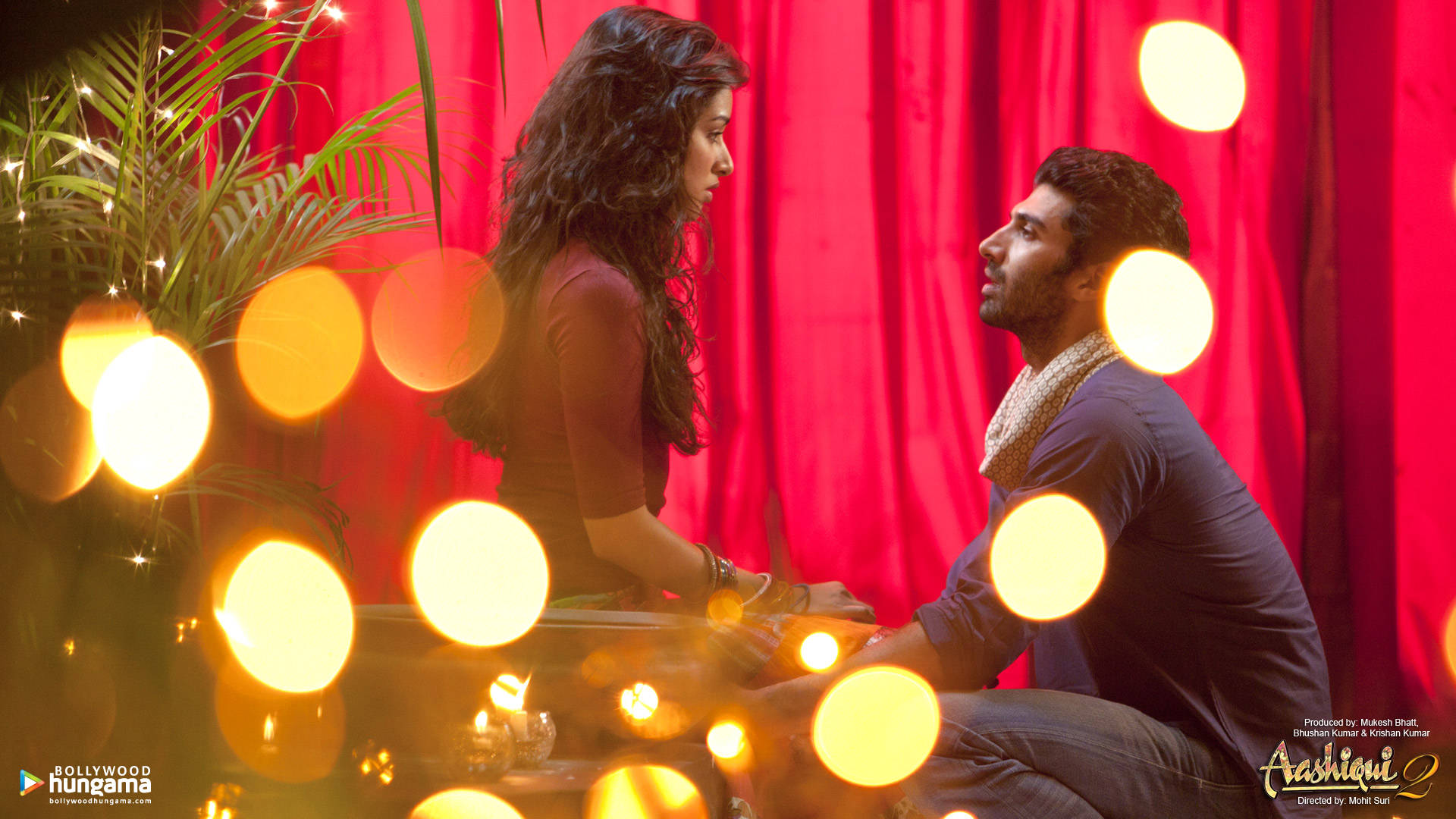 《Aashiqui 2》阿羅希與拉胡爾在紅色幕布上 壁紙 — 一對情侶在溫暖的散景燈光下，以豐富的紅色窗簾為背景，分享親密時刻。