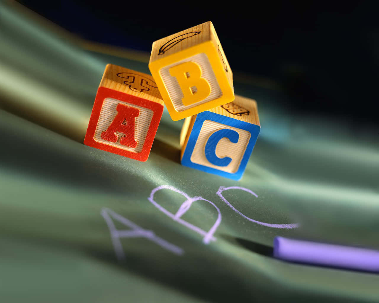 探索Abc的世界 壁紙 — 三個色彩繽紛的木製字母積木拼出ABC，放在綠色布料上，布料上有粉筆畫出的字母，附近還有一支紫色粉筆。