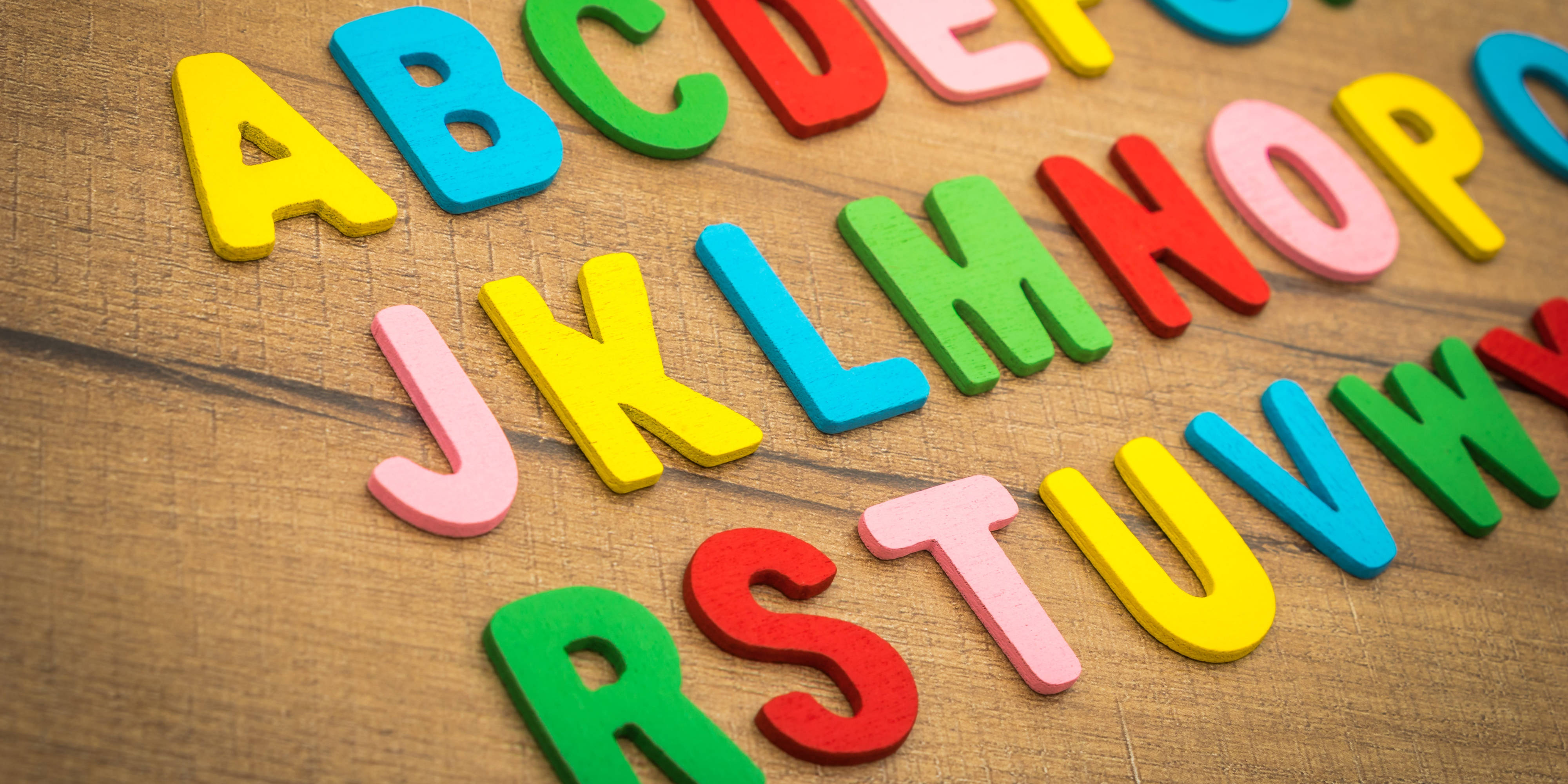ABC字母擺放在木桌上 壁紙 — 色彩繽紛的泡沫字母散落在溫暖的木質表面上，形成一個有趣的教學排列。