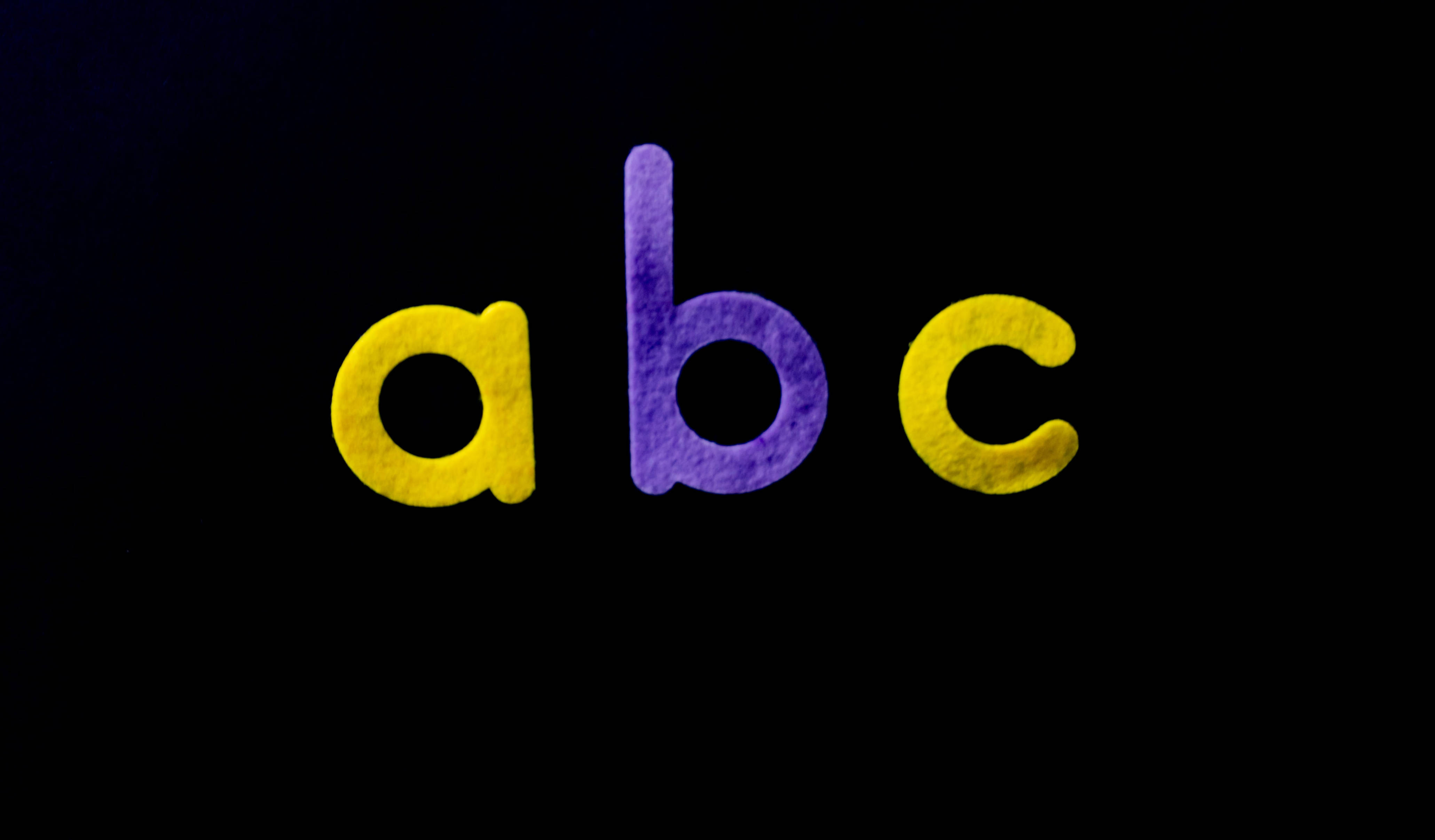 黃色與紫色的ABC字母 壁紙 — 粗體小寫字母 abc 在深黑色背景上發出紋理黃色和紫色的光芒。