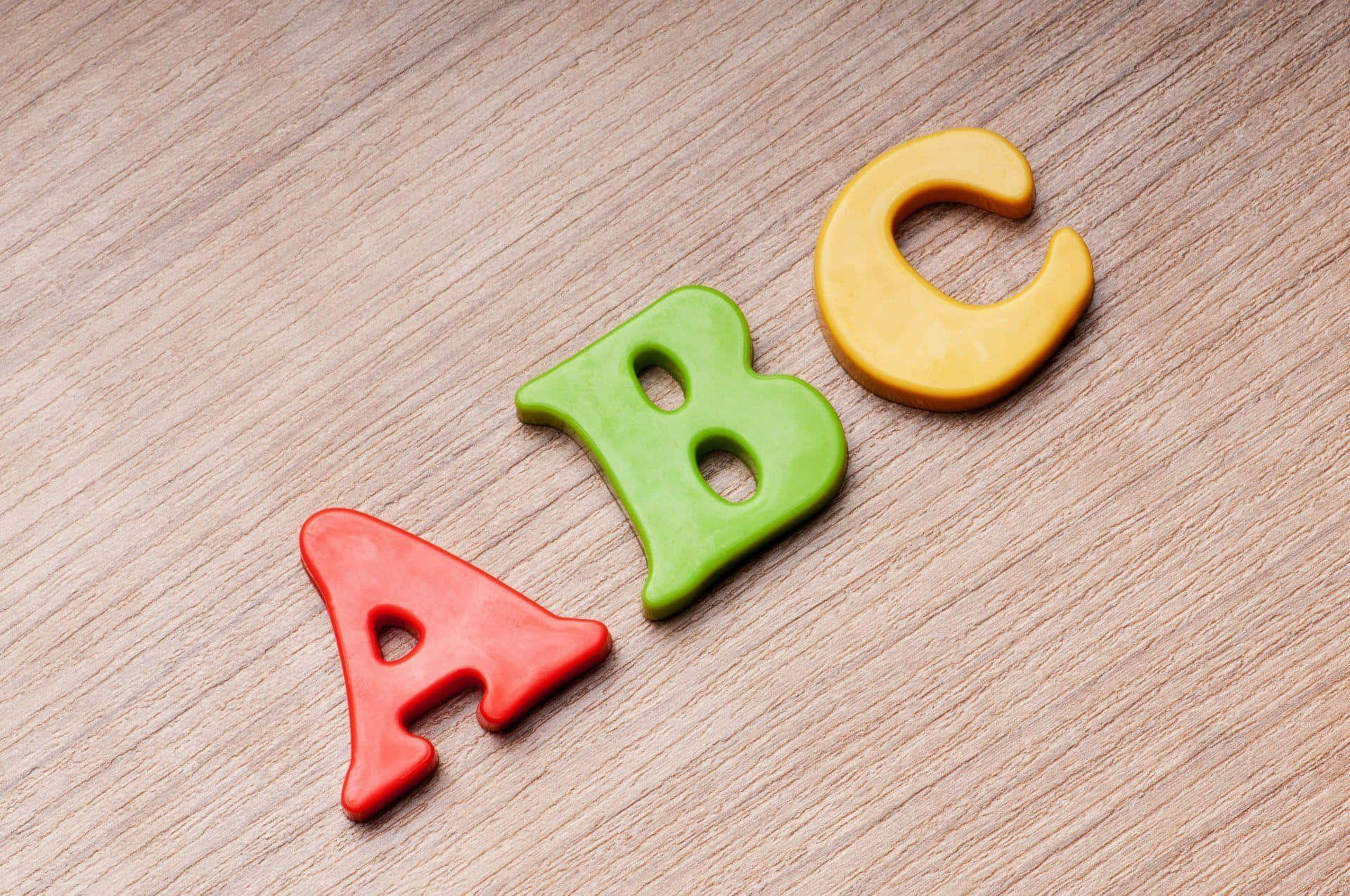 體驗ABC的刺激樂趣 壁紙 — 三個色彩繽紛的黏土字母ABC對角排列在淺色木質表面上。