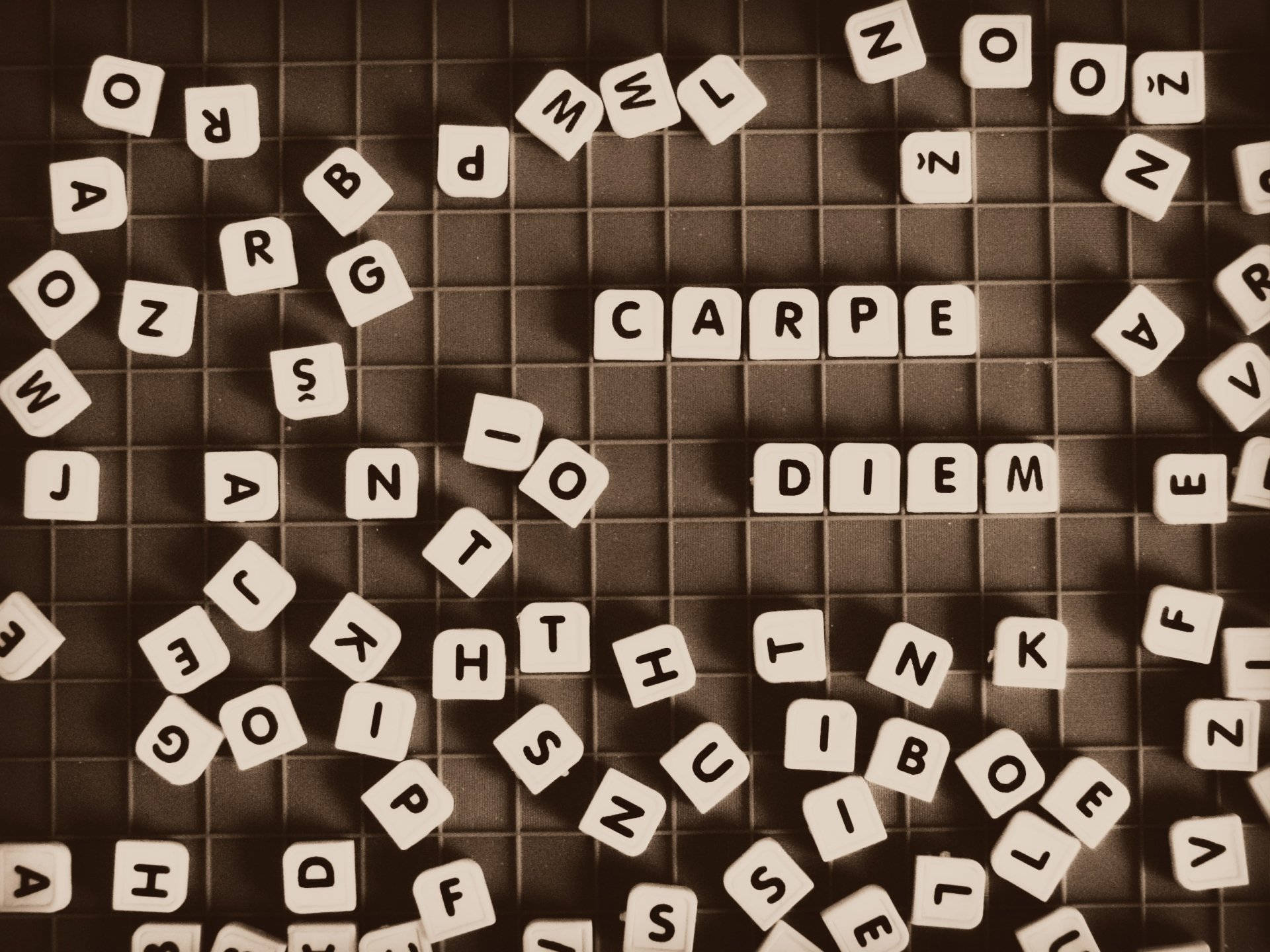 ABC Scrabble字母方塊 壁紙 — 散落在網格上的字母瓷磚以懷舊棕色調拼出「CARPE DIEM」，周圍散落著字母。