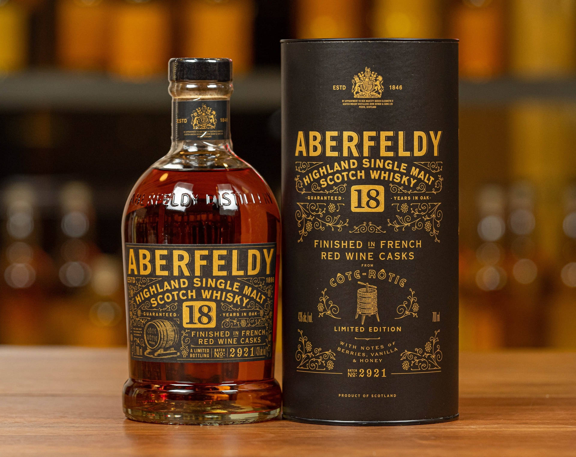 Aberfeldy 18年威士忌酒瓶和盒子放在木桌上，後面有模糊的琥珀色瓶子。