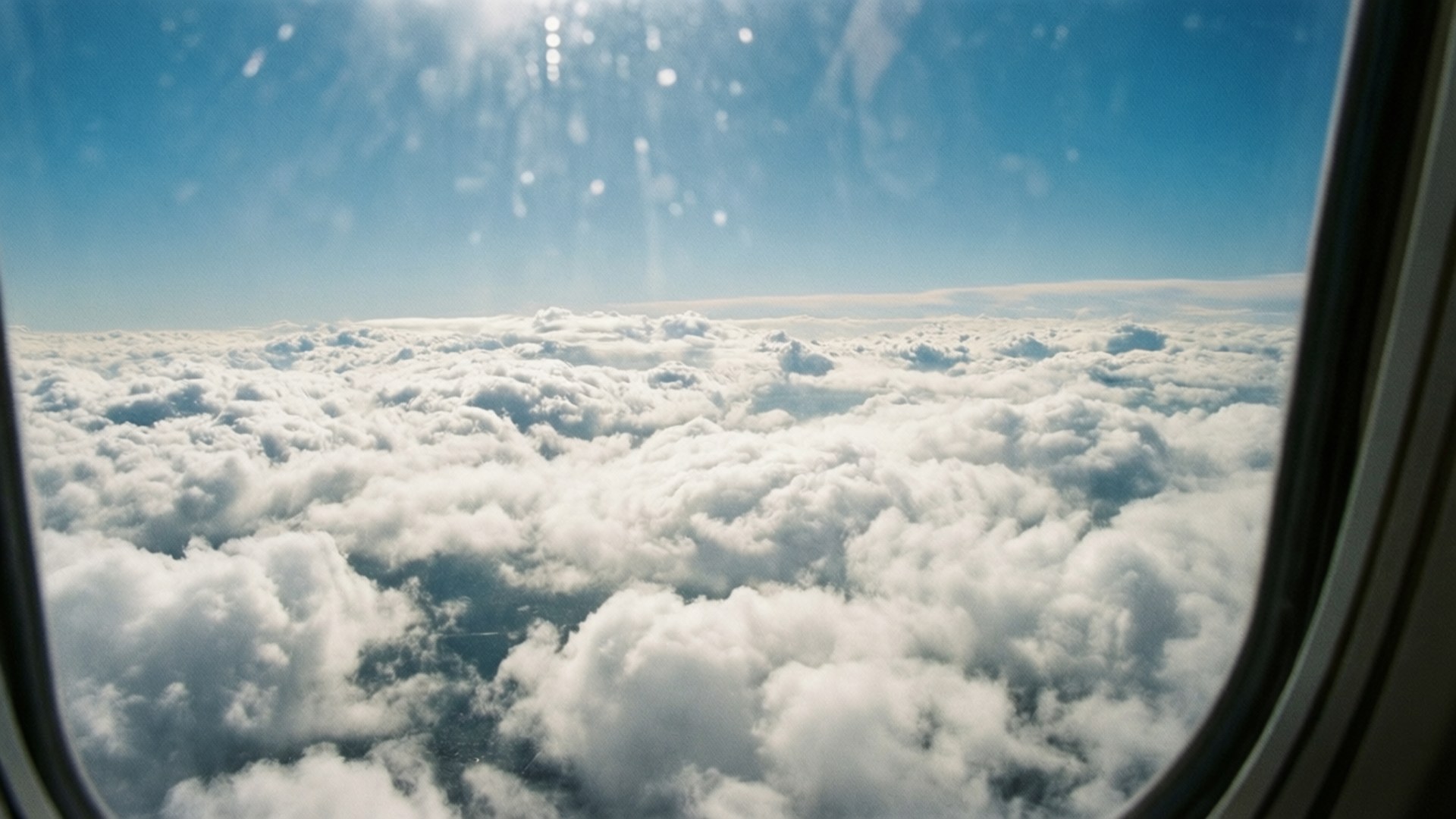 從飛機窗戶俯瞰蓬鬆白雲的空中景色，明亮的藍天和太陽耀斑