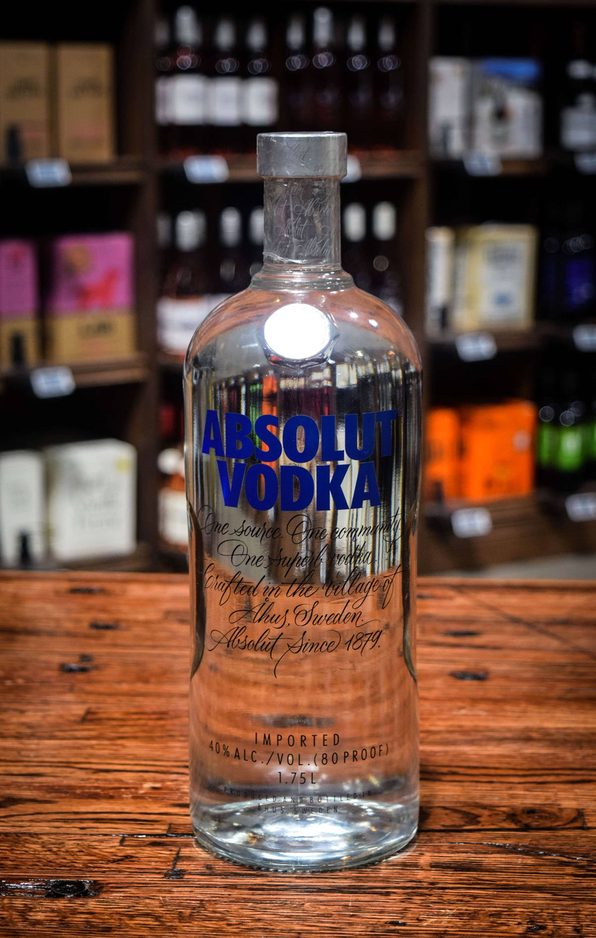 透明Absolut Vodka樽喺木吧枱上，後面有酒架。