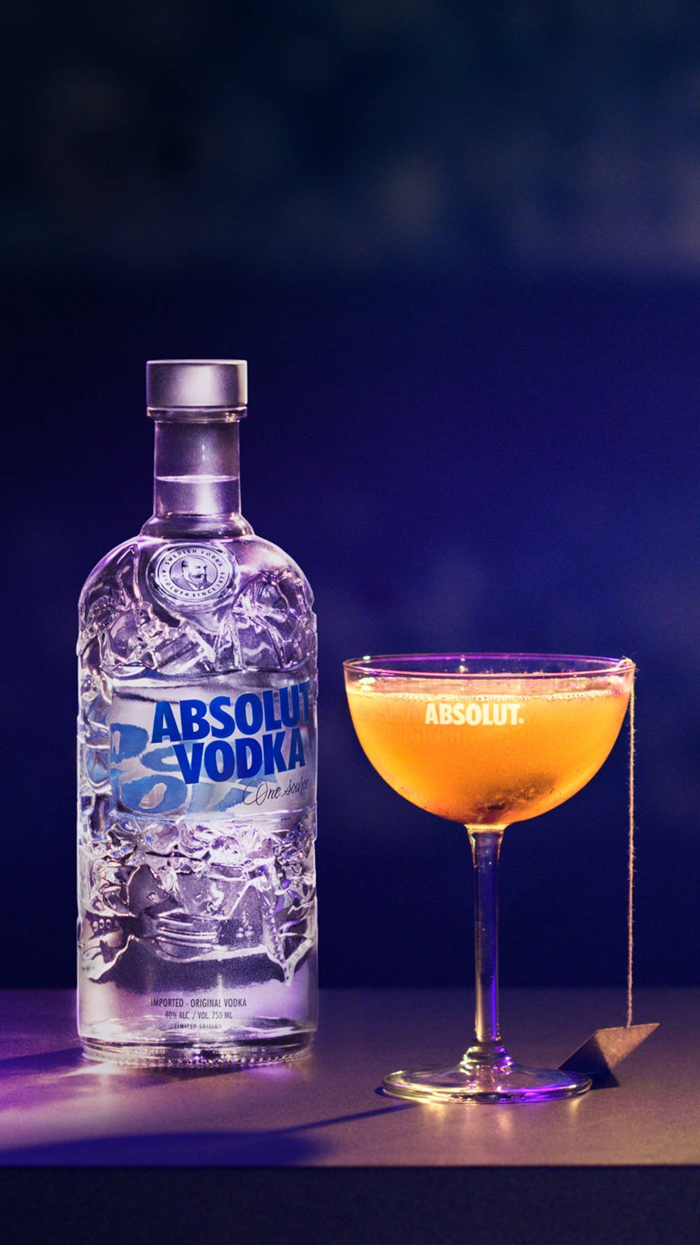 Absolut Vodka 瓶和雞尾酒在深色表面上，紫色燈光下。
