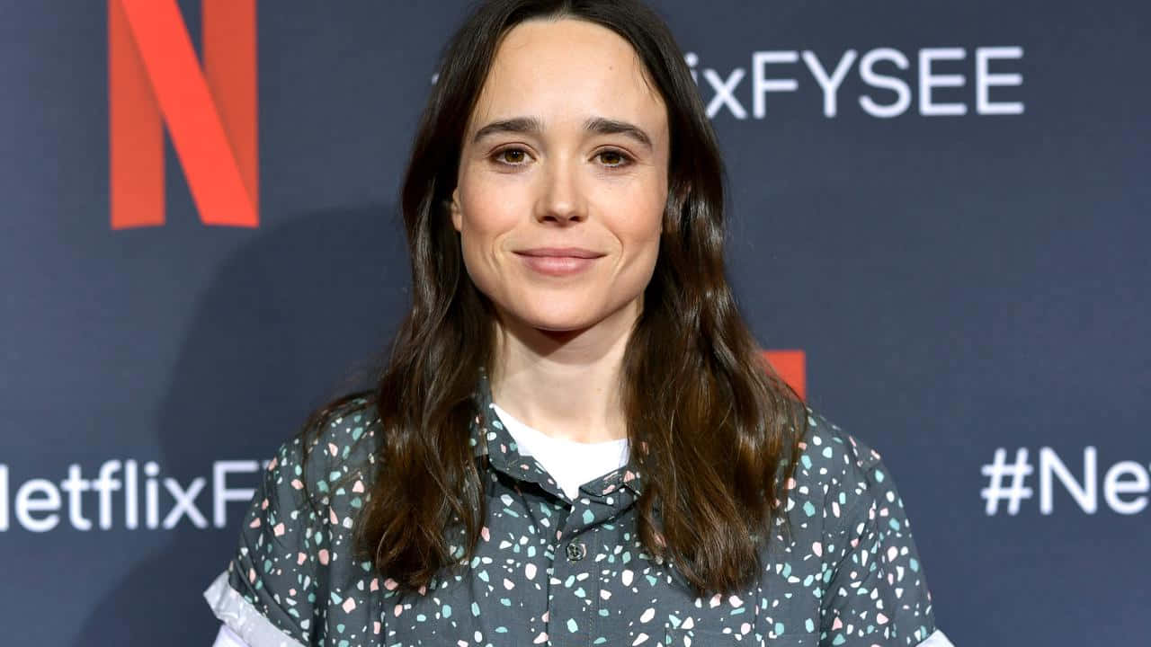  壁紙 — 女演員艾倫佩姬在Netflix活動背景下穿著圖案襯衫對著鏡頭溫柔微笑。