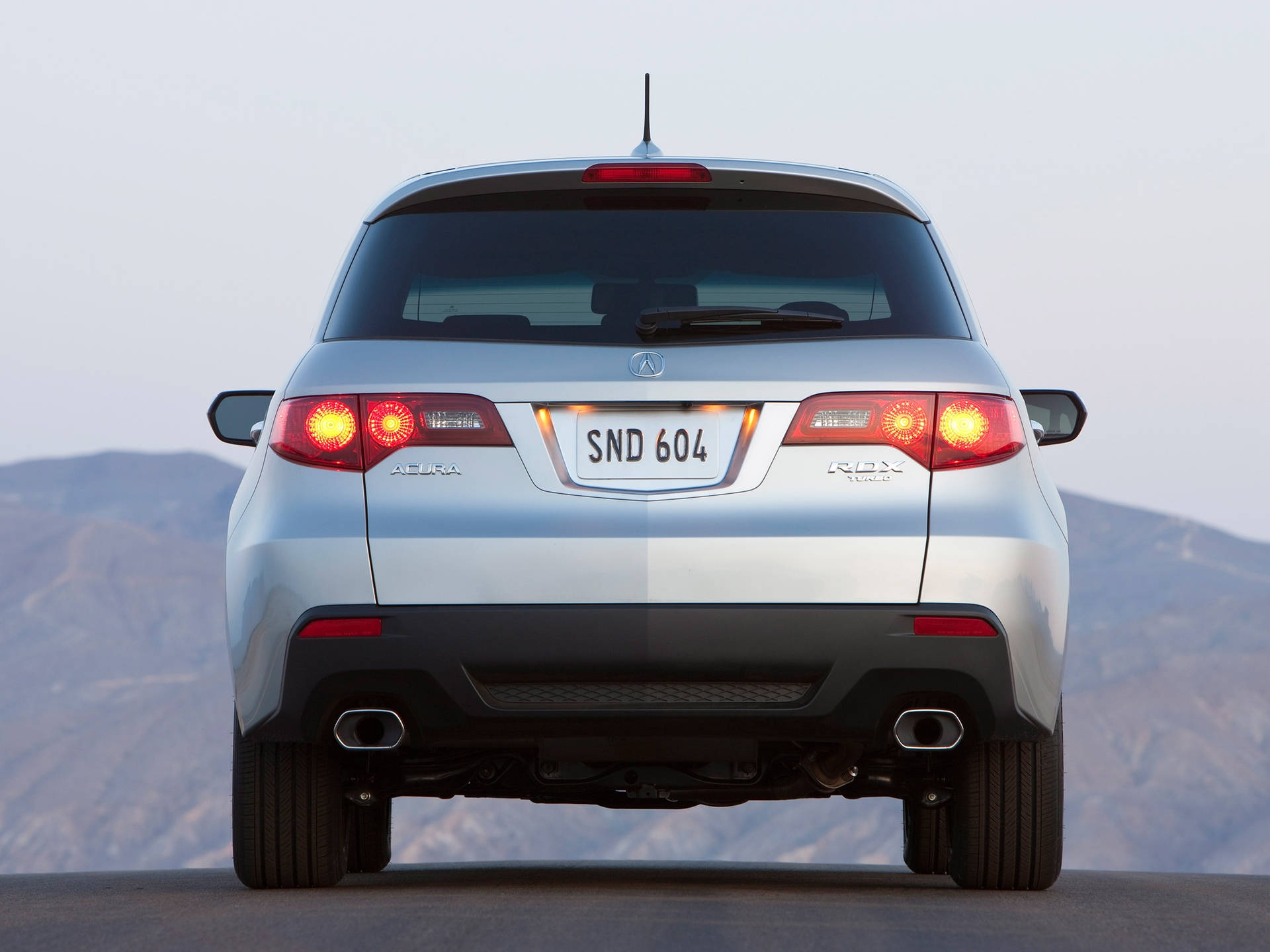 銀色Acura RDX SUV後視圖，黃昏的山路上發光的尾燈。
