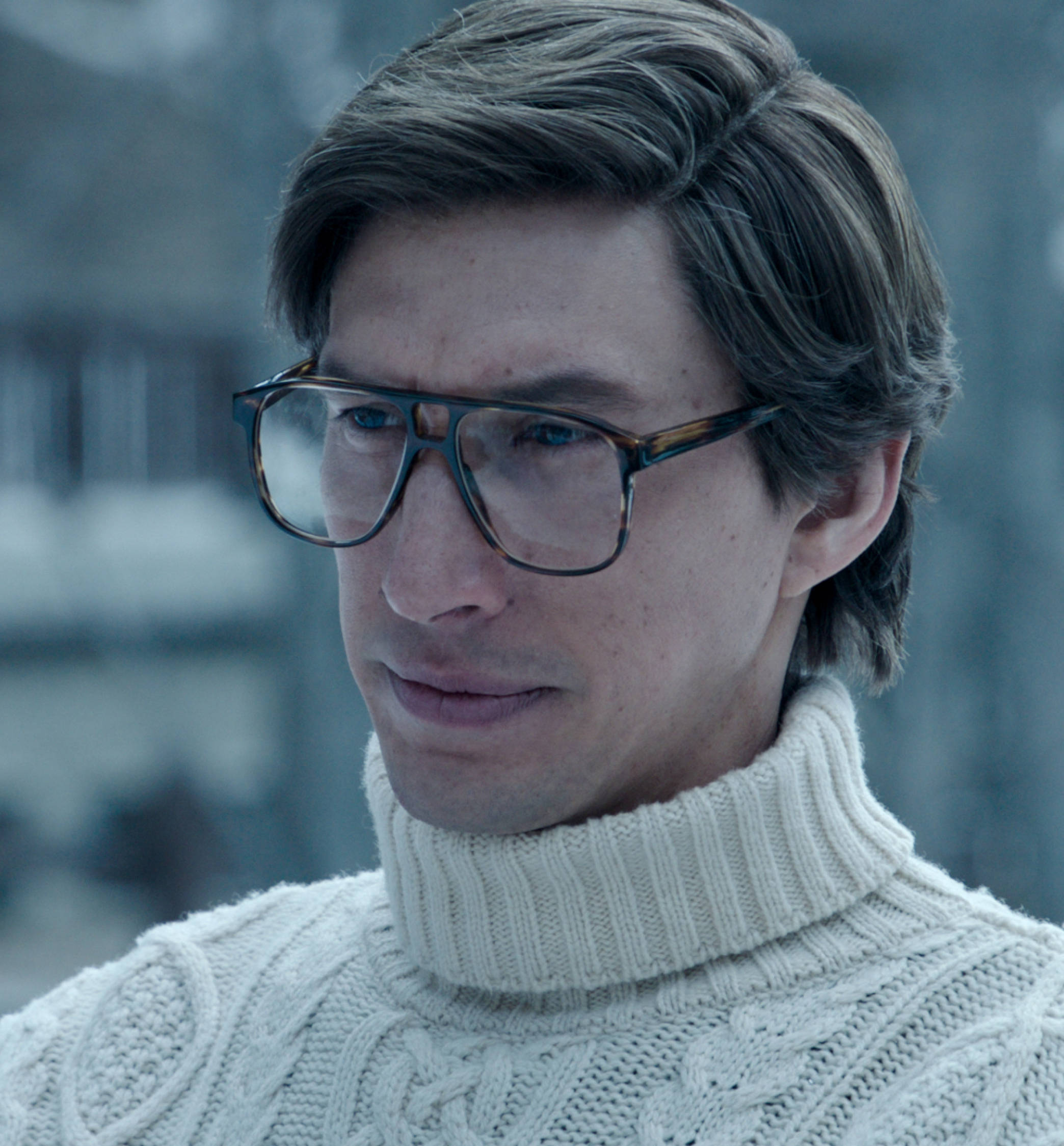 古驰家族 Adam Driver 近照 壁紙 — 一個戴眼鏡、身穿米色高領毛衣的男人，在模糊的冬日背景下若有所思地凝視著。