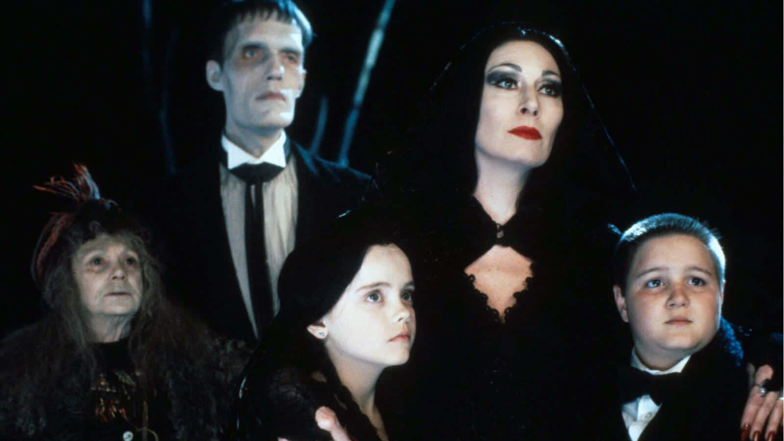 《Addams Family》：古怪從未如此迷人 壁紙 — 阿達一族以哥德式黑色服裝在黑暗背景下擺姿勢，燈光效果戲劇性。