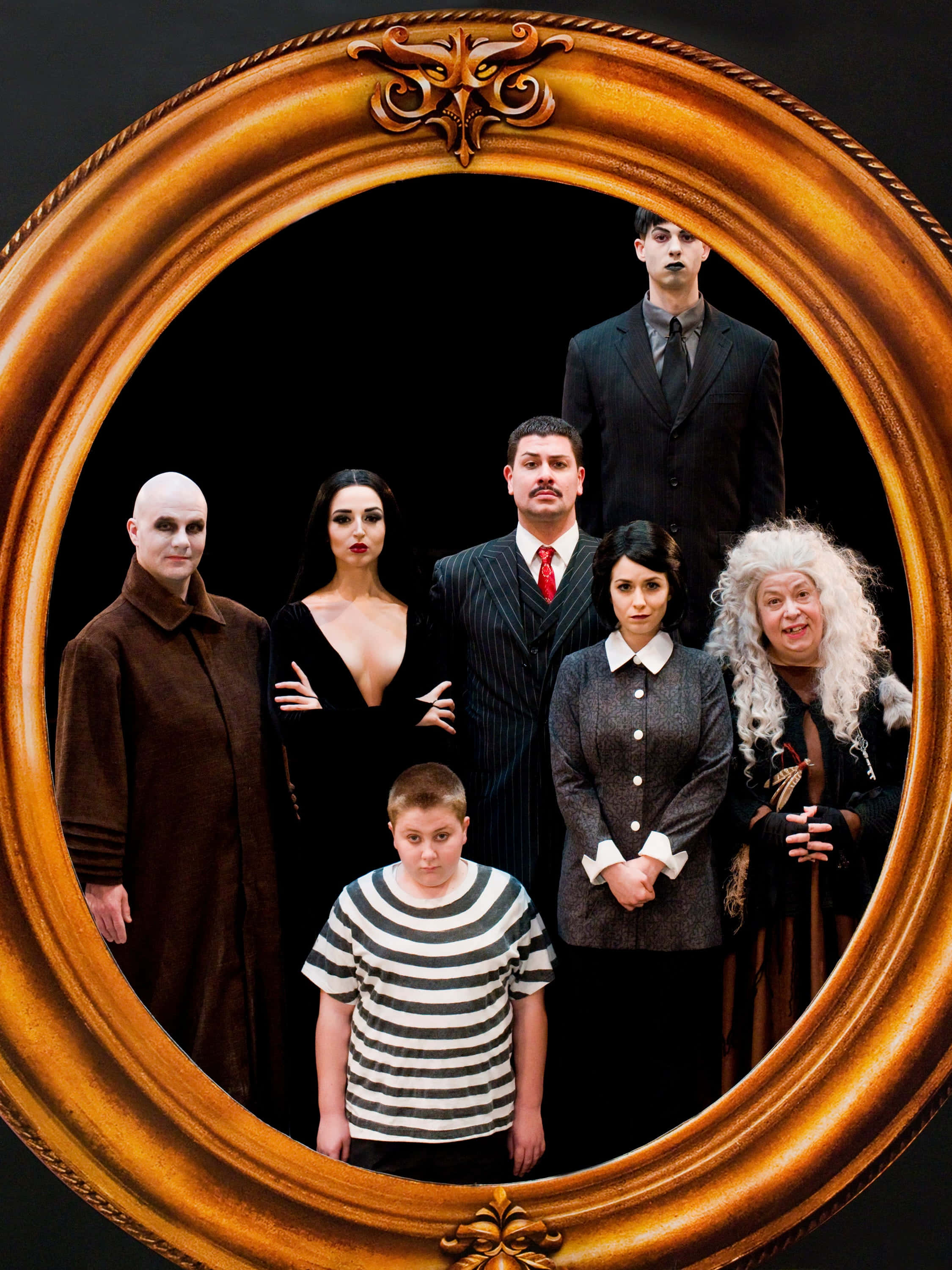 《Addams Family》過著詭異的生活 壁紙 — 一個華麗金色畫框中的哥德式家庭肖像，七個角色穿著戲劇性服裝，背景為黑色。