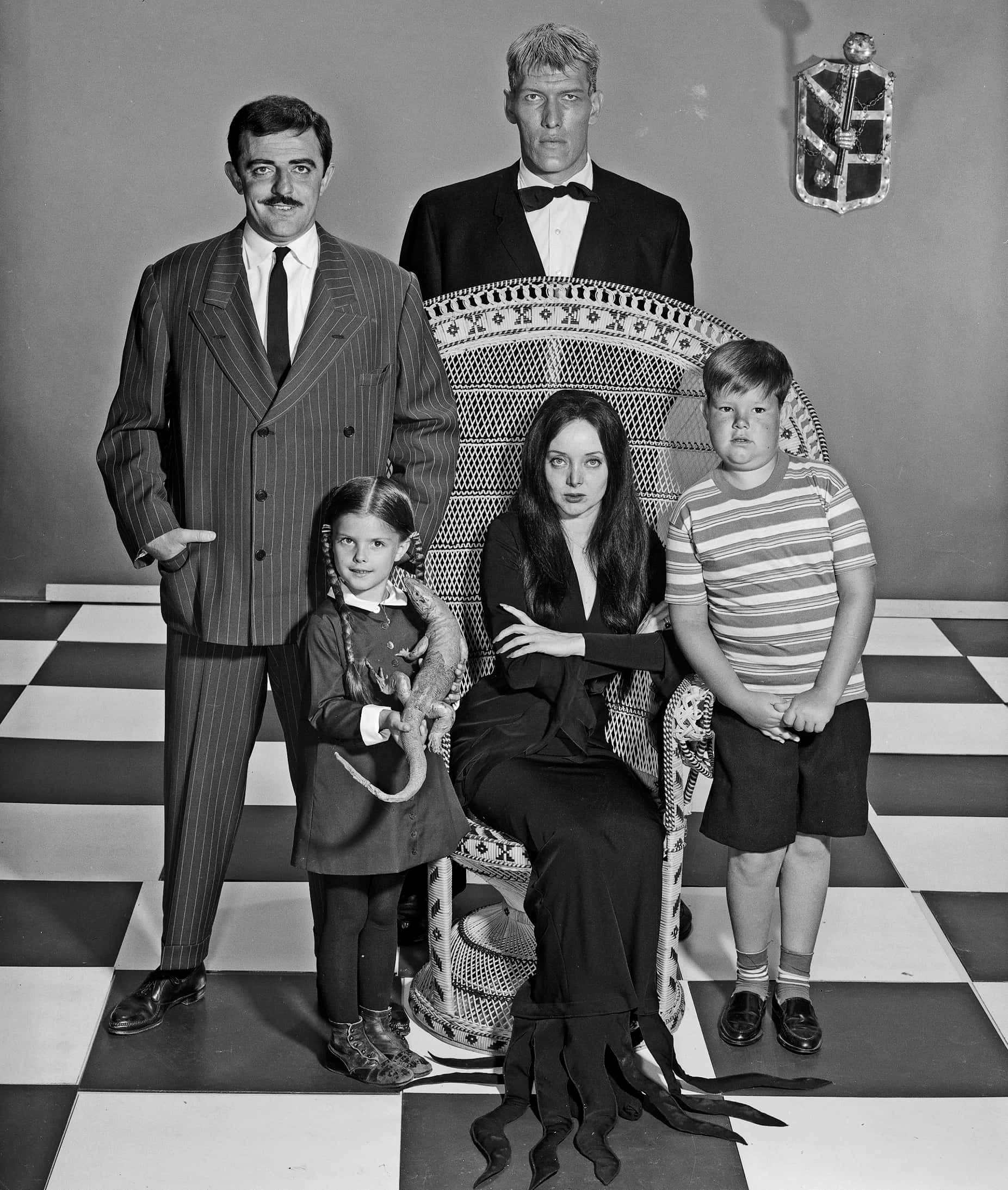 Addams家族 - Lurch、Gomez、Morticia、Wednesday與Pugsley 壁紙 — 阿達一族在棋盤格地板上的黑白家庭肖像，帶有哥德式裝飾。