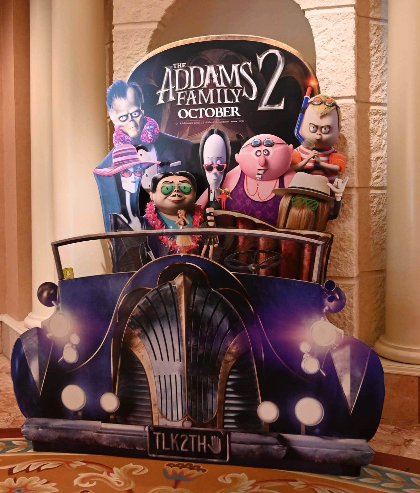 Addams家族合照 壁紙 — 一個充滿活力的3D宣傳剪紙，展示The Addams Family 2角色在紫色復古車中，車牌為'TLK2TH'。