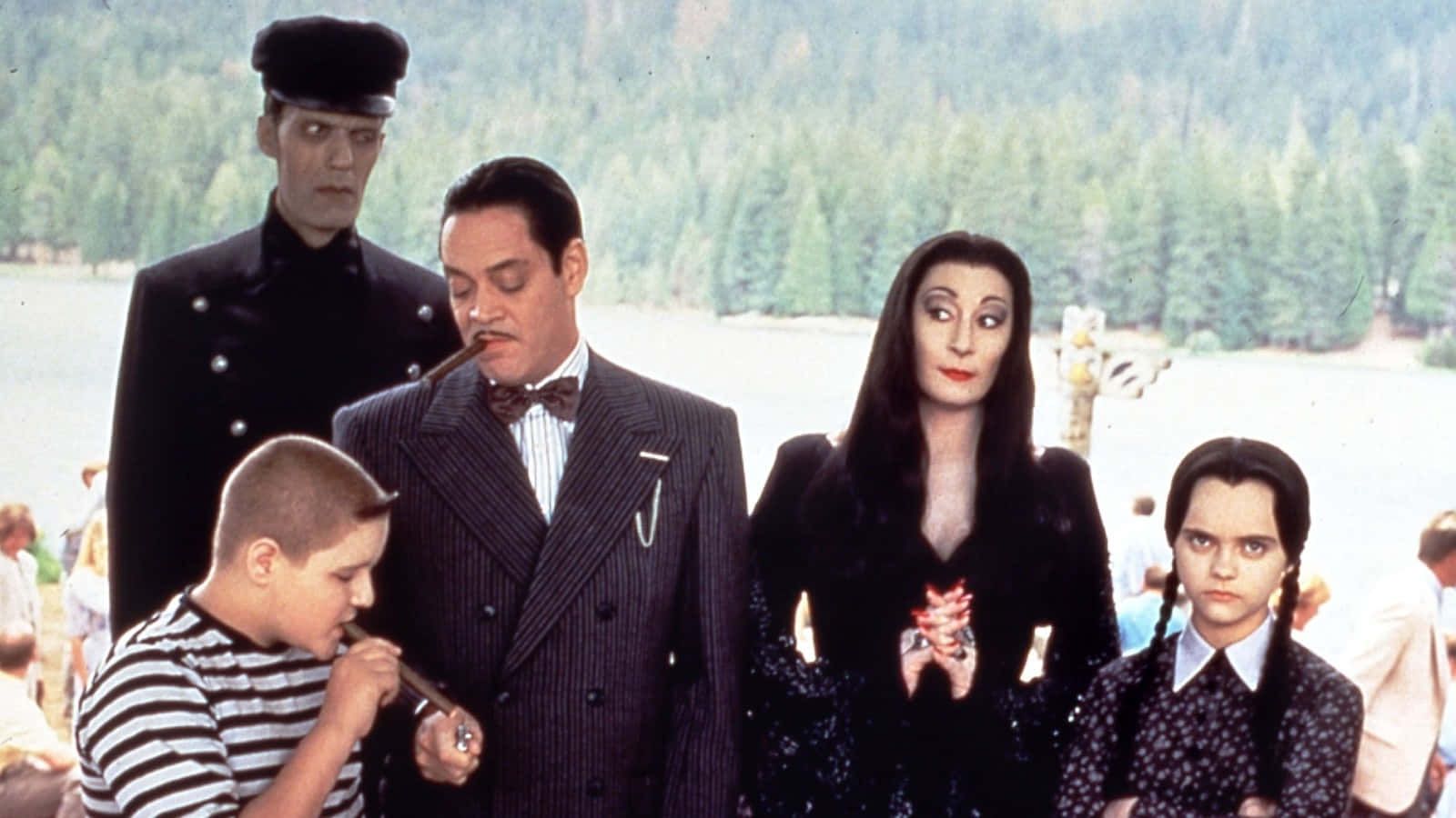Addams家族的日常趣事 壁紙 — 阿達一族莊嚴地站在湖邊，身後是樹木繁茂的山丘，身穿他們標誌性的暗黑哥德式服裝。