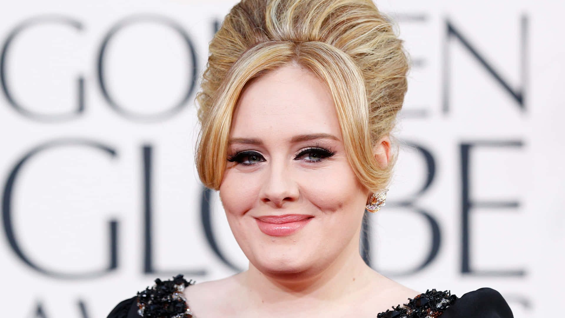 Adele 在金球獎上穿著黑色鑲飾連衣裙微笑。