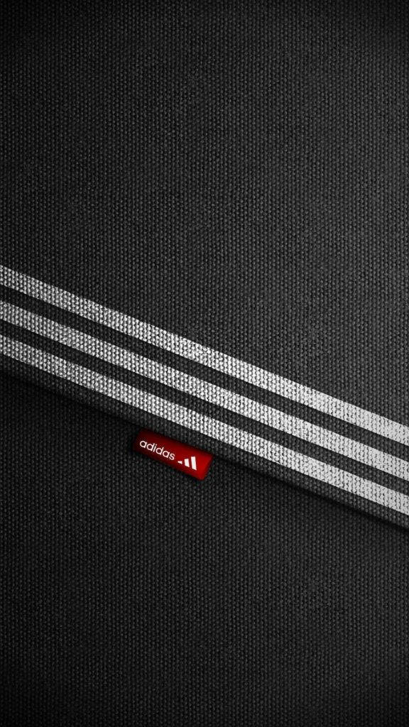 Adidas iPhone 標誌布料紋理背景 壁紙 — 黑色紋理布料特寫，帶有白色條紋和紅色 adidas 標誌標籤。