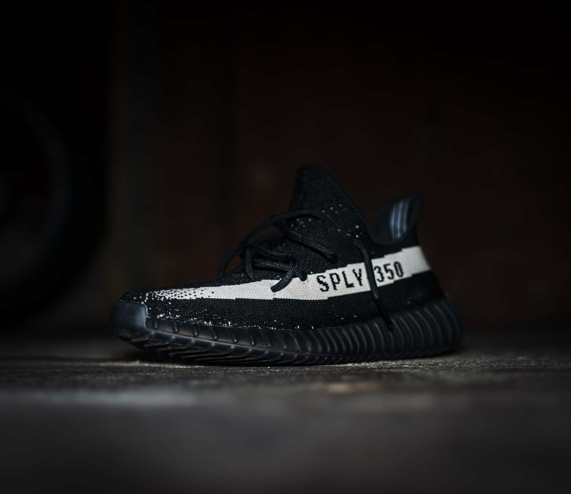 昏暗光線下，混凝土地板上的黑色Yeezy Boost 350運動鞋，帶有白色條紋。