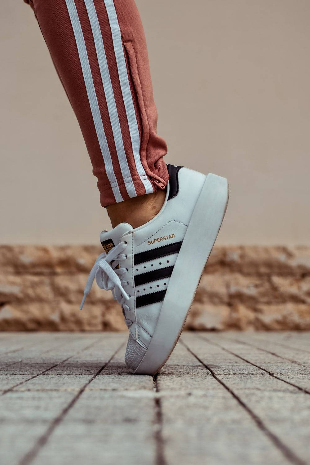 白色 adidas superstar 運動鞋在石頭路面上的特寫，搭配鏽色運動褲。