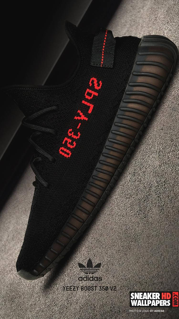 灰色地毯上的黑色Yeezy Boost 350 V2運動鞋，帶有紅色文字。