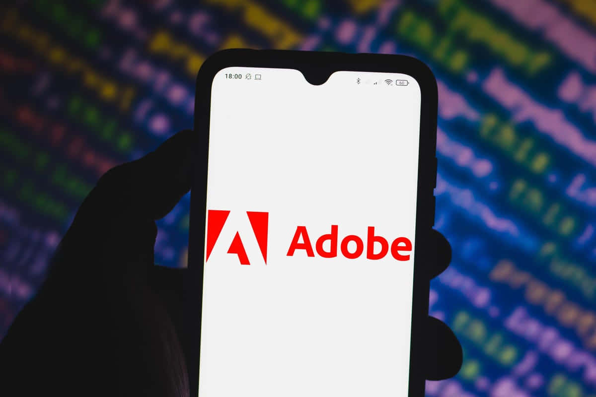 手拿著帶有Adobe標誌和發光代碼背景的電話。
