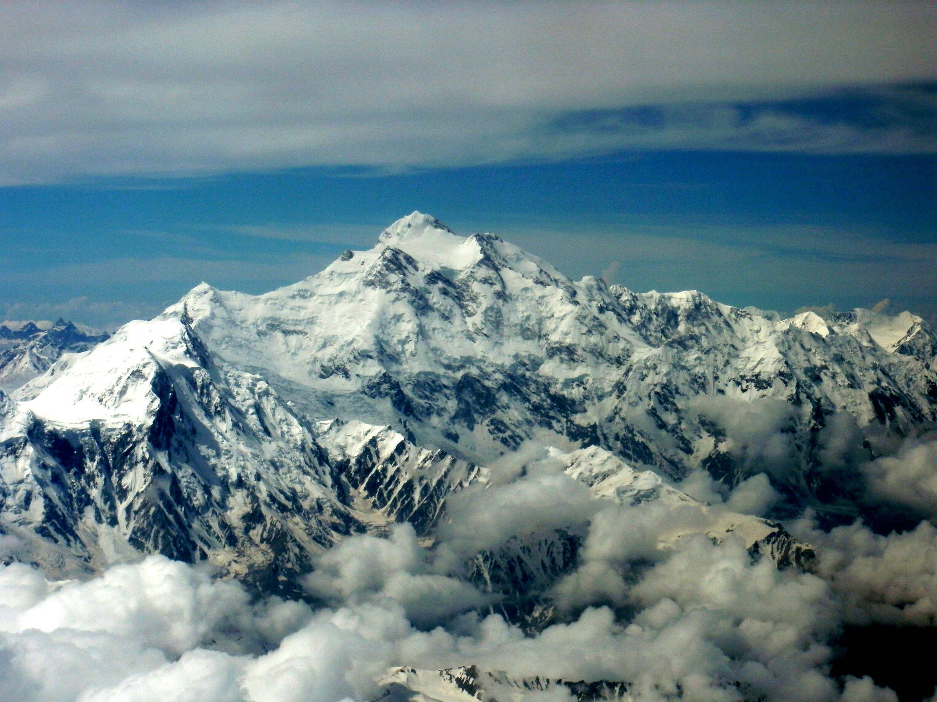 積雪的山峰聳立於雲層之上，藍天為背景