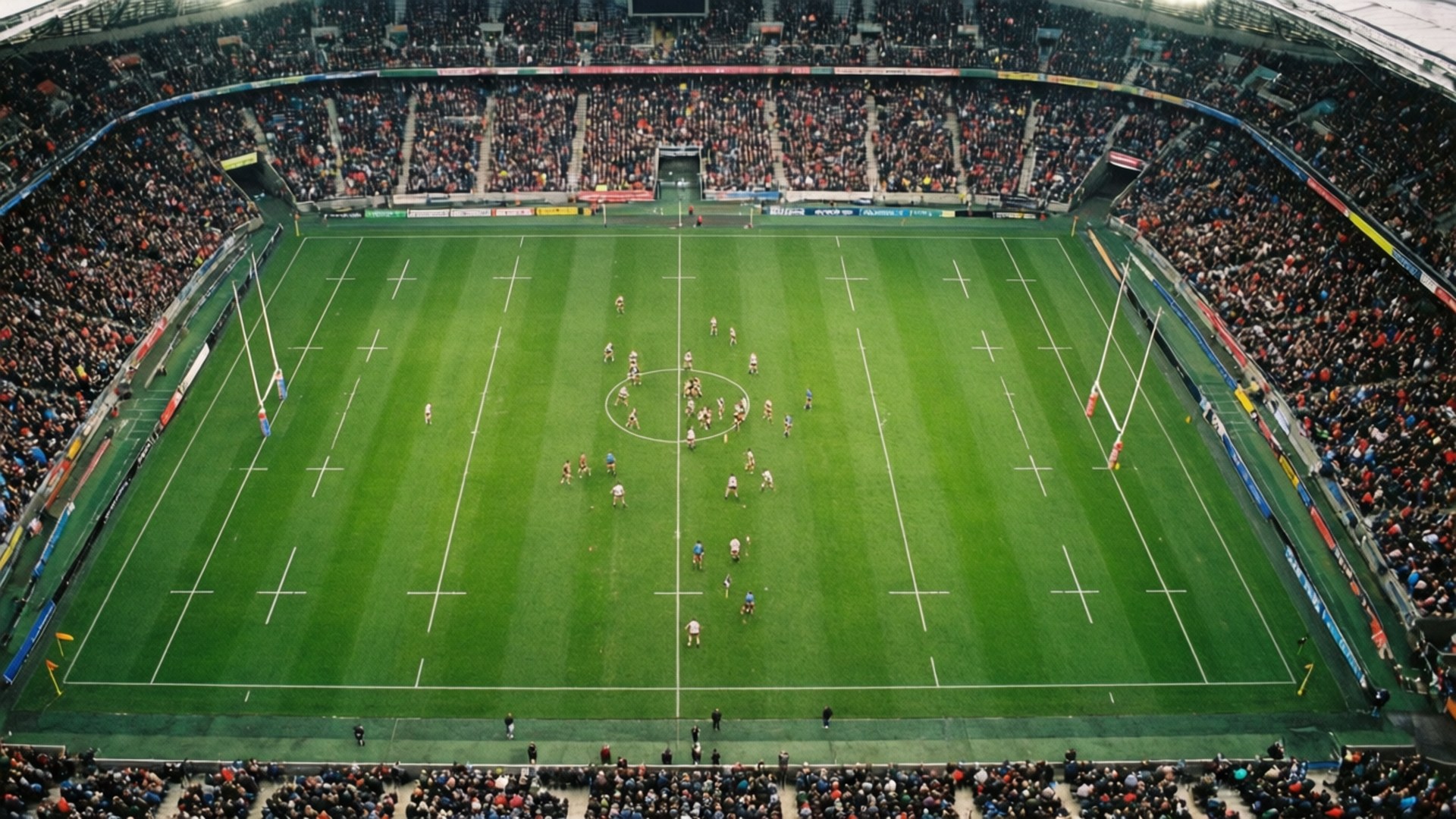 Rugby 桌布 壁紙 — 從高空俯瞰一個擠滿觀眾的體育場內，欖球比賽正在進行，球員在充滿活力的綠色場地上激烈角逐。