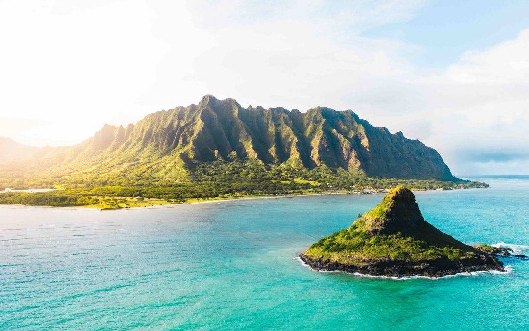 奧胡島日落島嶼 壁紙 — 從高空俯瞰，翠綠的山巒從碧綠的海水中升起，前景有一個小島。