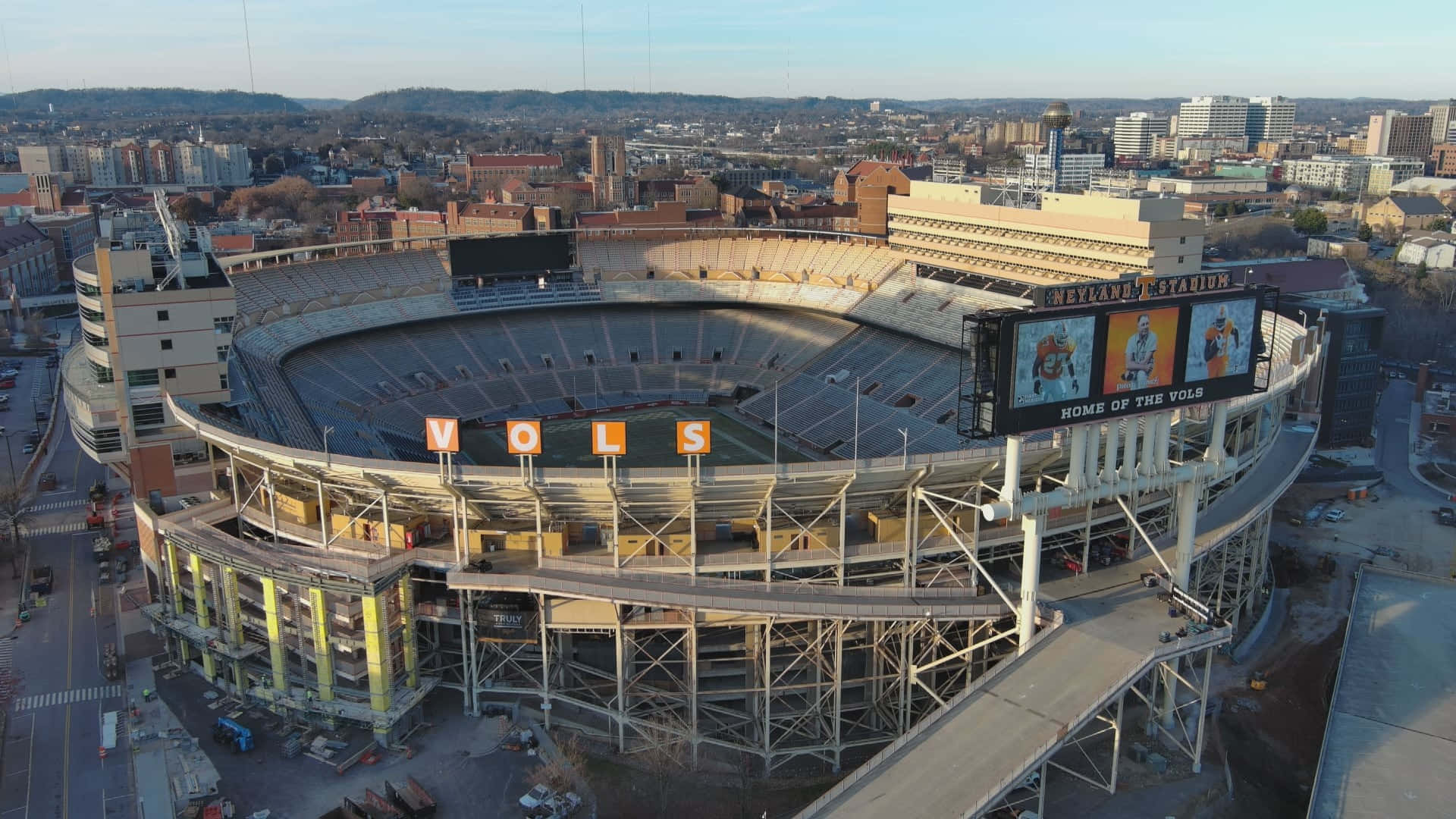  壁紙 — Neyland Stadium 施工中的鳥瞰圖，背景有「VOLS」標誌和城市景觀，日出時分。