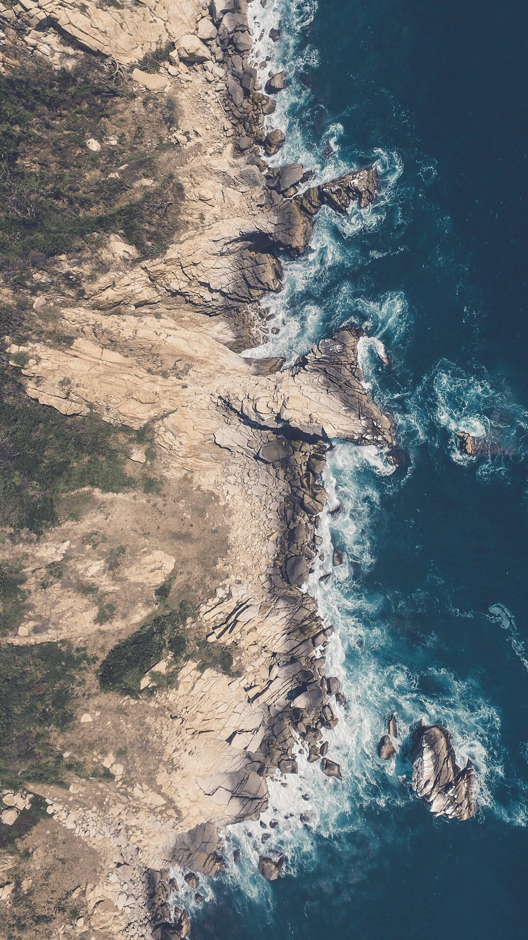 從上方俯瞰，崎嶇的海岸懸崖，海浪拍打，植被稀疏。