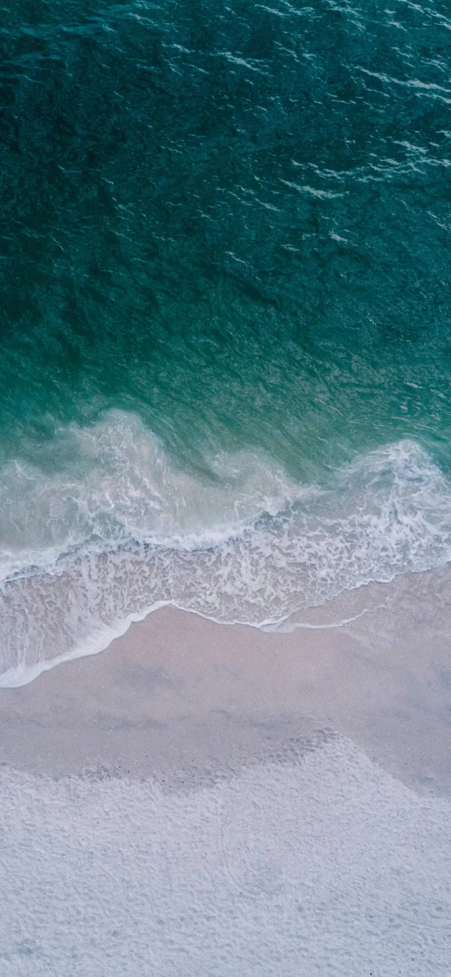 從上方看到綠松石色的海浪與粉色沙灘在海岸線交匯。
