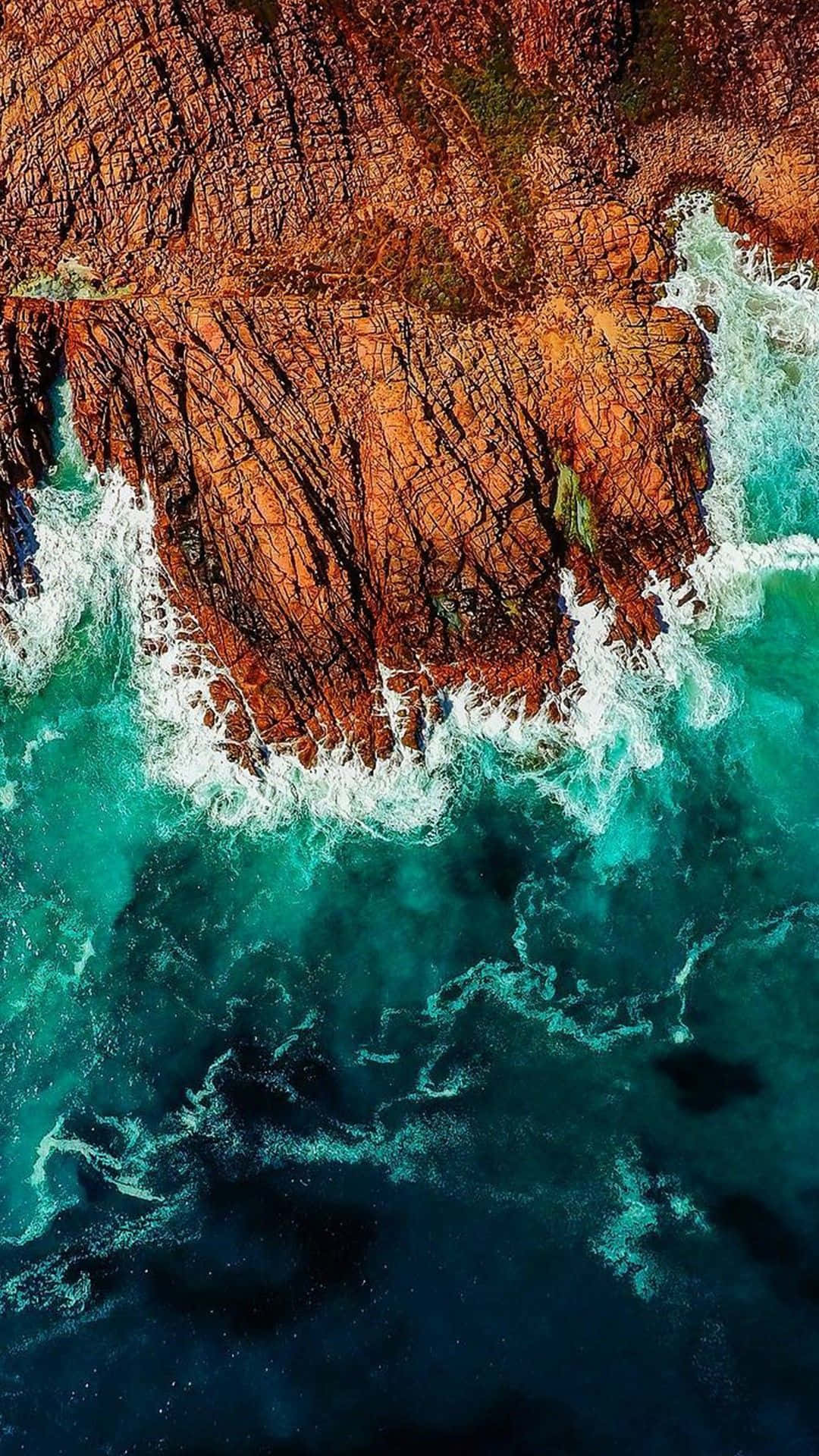 waves 桌布 壁紙 — 從高空俯瞰，藍綠色海浪拍打著崎嶇的橙色懸崖，激起白色泡沫。