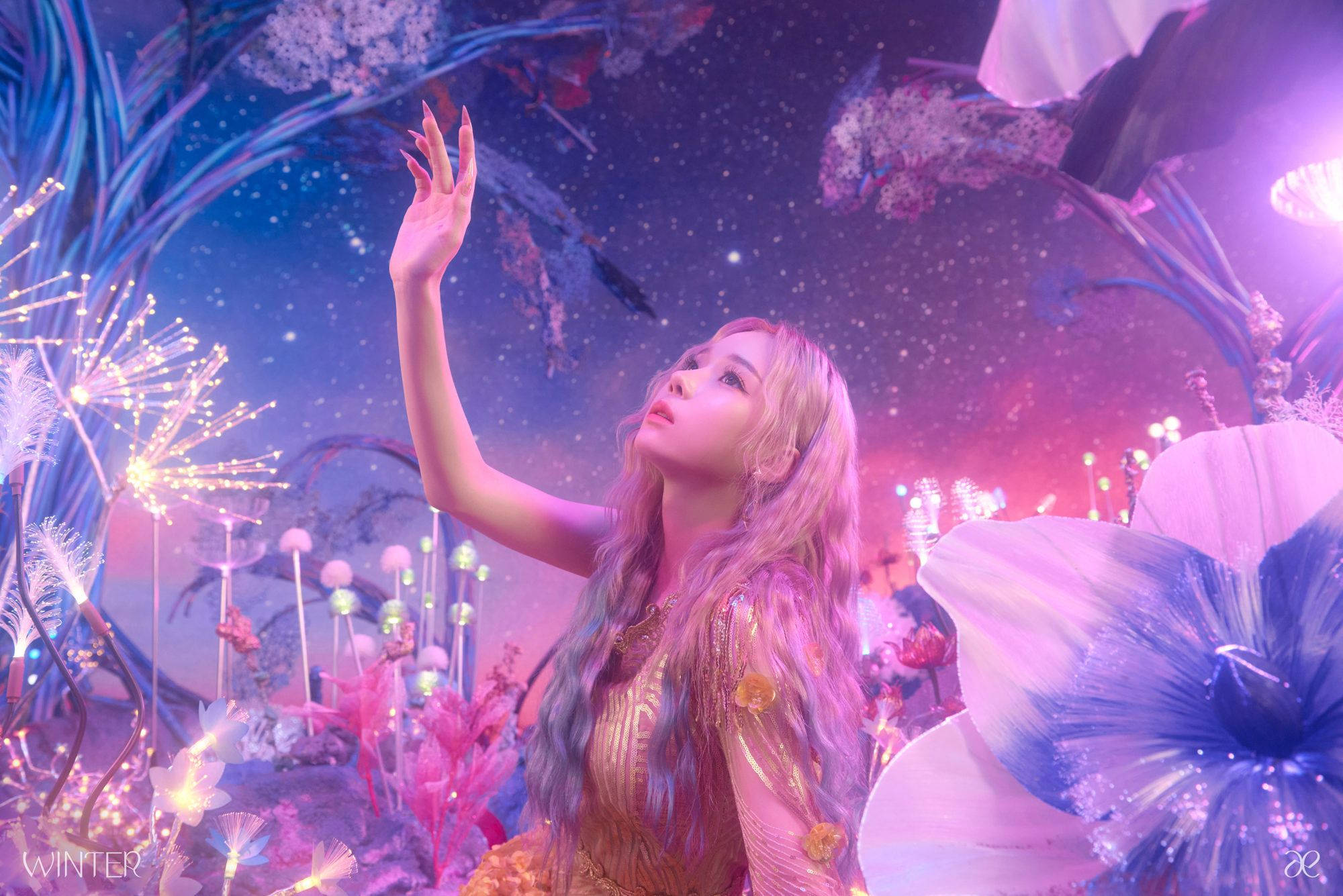 Aespa 冬日璀璨風景 壁紙 — 一位長金髮的女性在一個超現實的花園中向上伸手，花園在星空下閃爍著紫色、粉紅色和藍色的光芒。