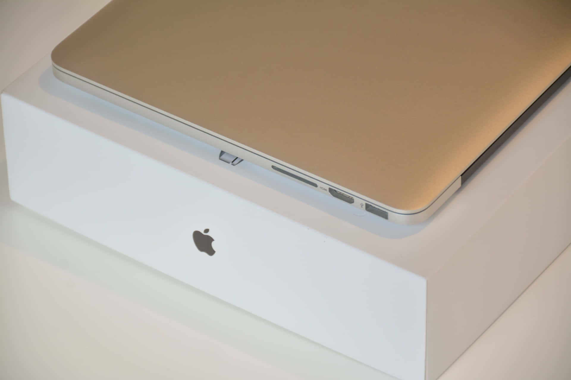 金色 MacBook 放在白色 Apple 盒上，顯示連接埠和標誌